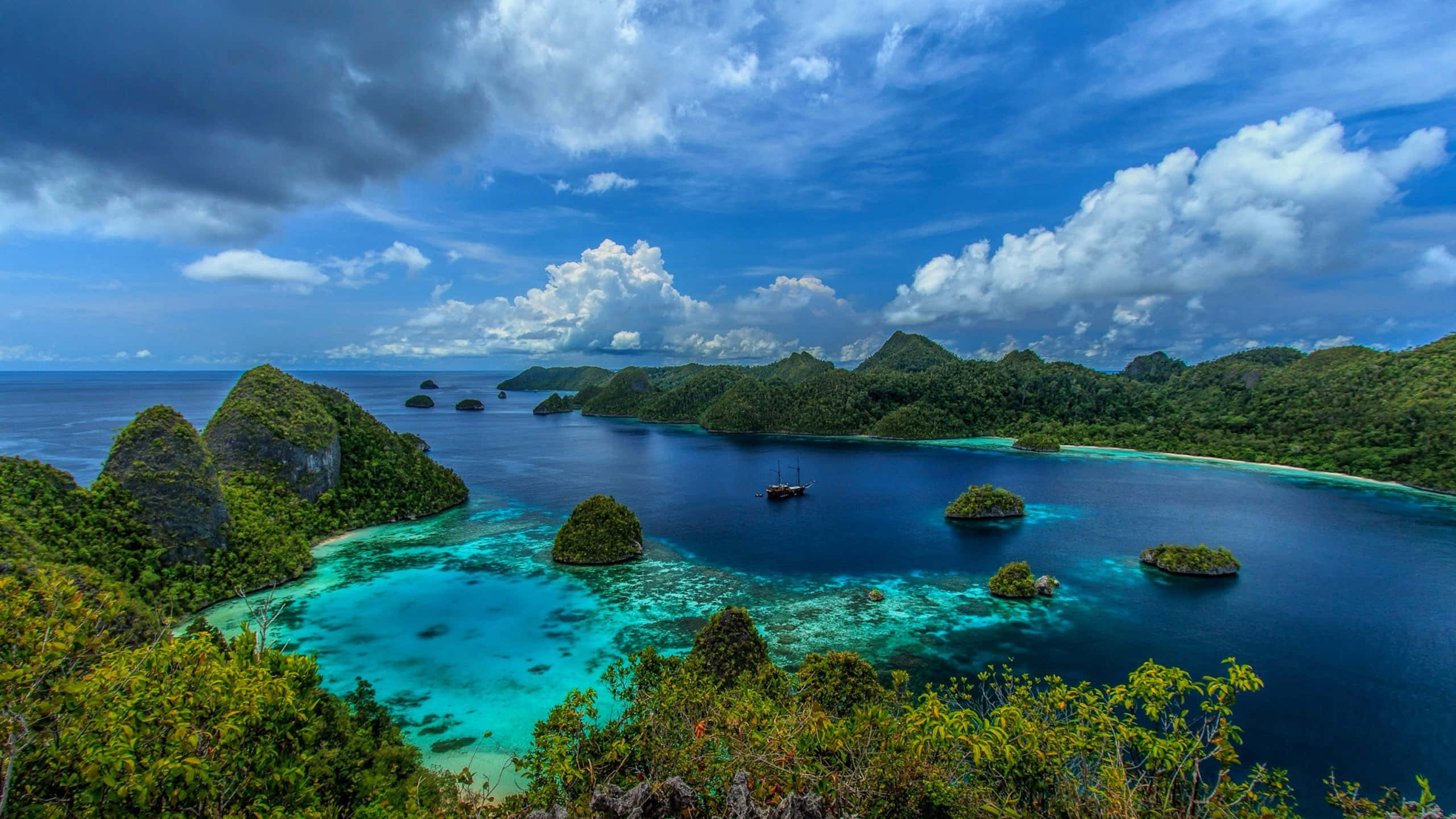Indonesia 桌布 壁紙 — 一個令人嘆為觀止的熱帶海灣，擁有翠綠的小島和碧綠的海水，在戲劇性的藍天和白雲下。
