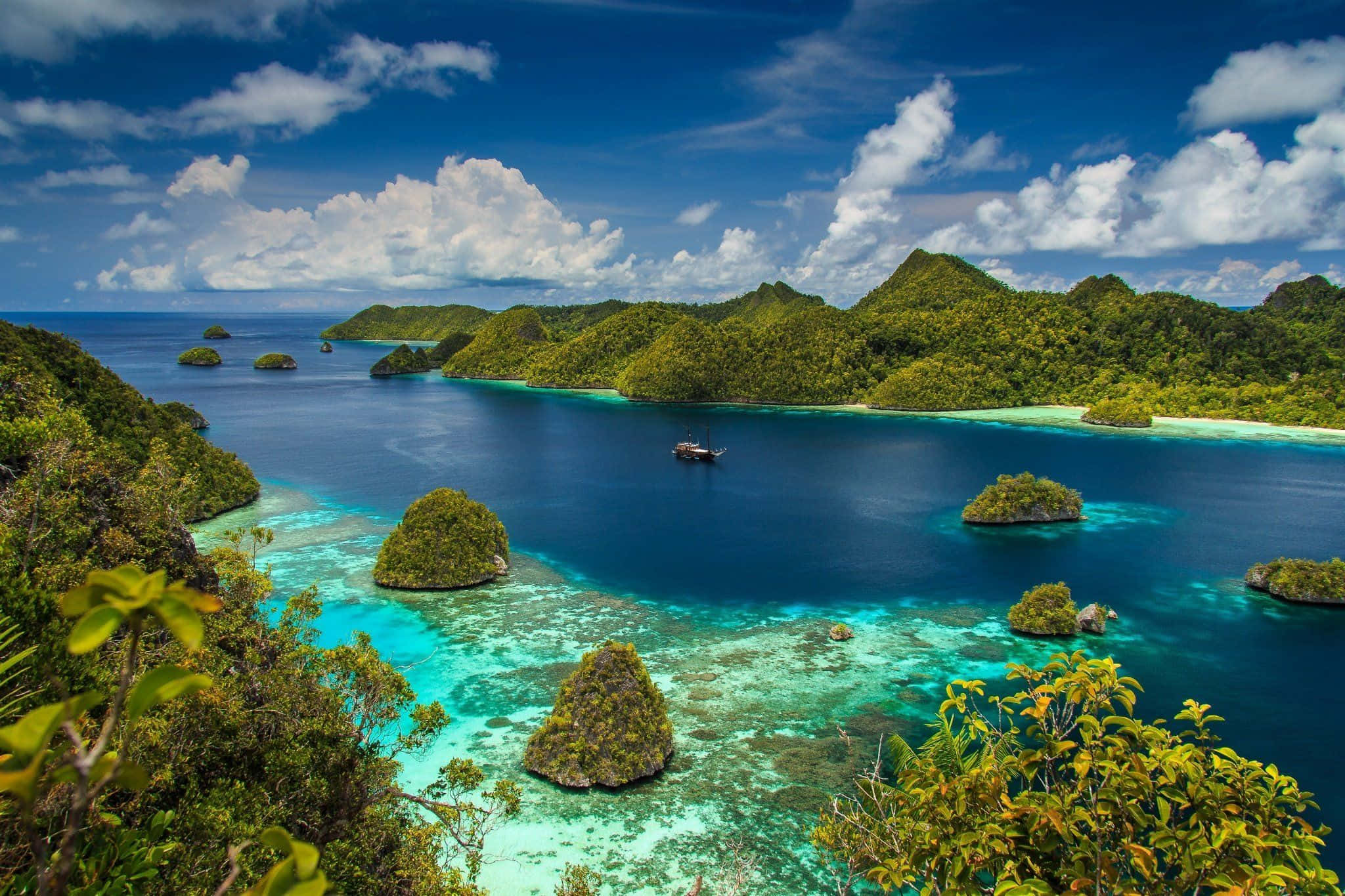 Indonesia 桌布 壁紙 — 一個令人嘆為觀止的熱帶海灣，翡翠色的小島和碧綠的海水，在湛藍的天空和蓬鬆的白雲下。