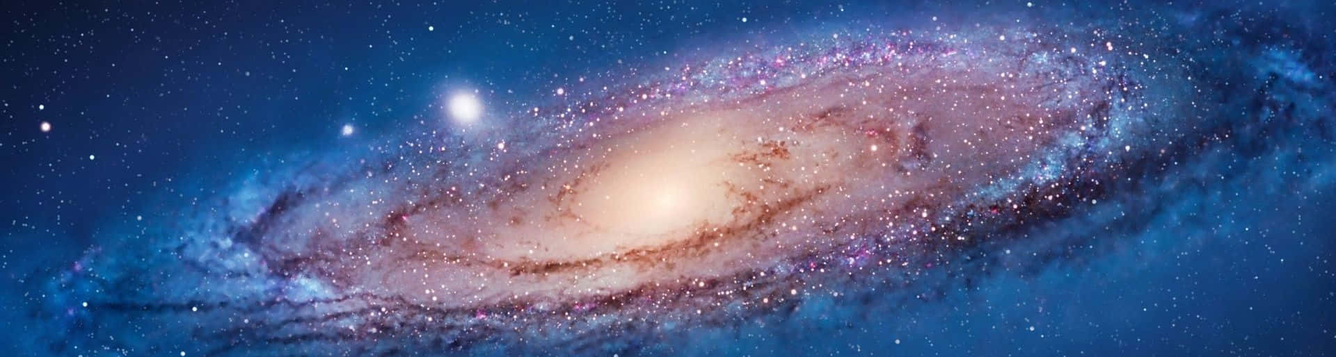 雙螢幕 桌布 壁紙 — 一個令人嘆為觀止的螺旋星系，在深藍色的虛空中旋轉著宇宙塵埃和閃爍的星星。