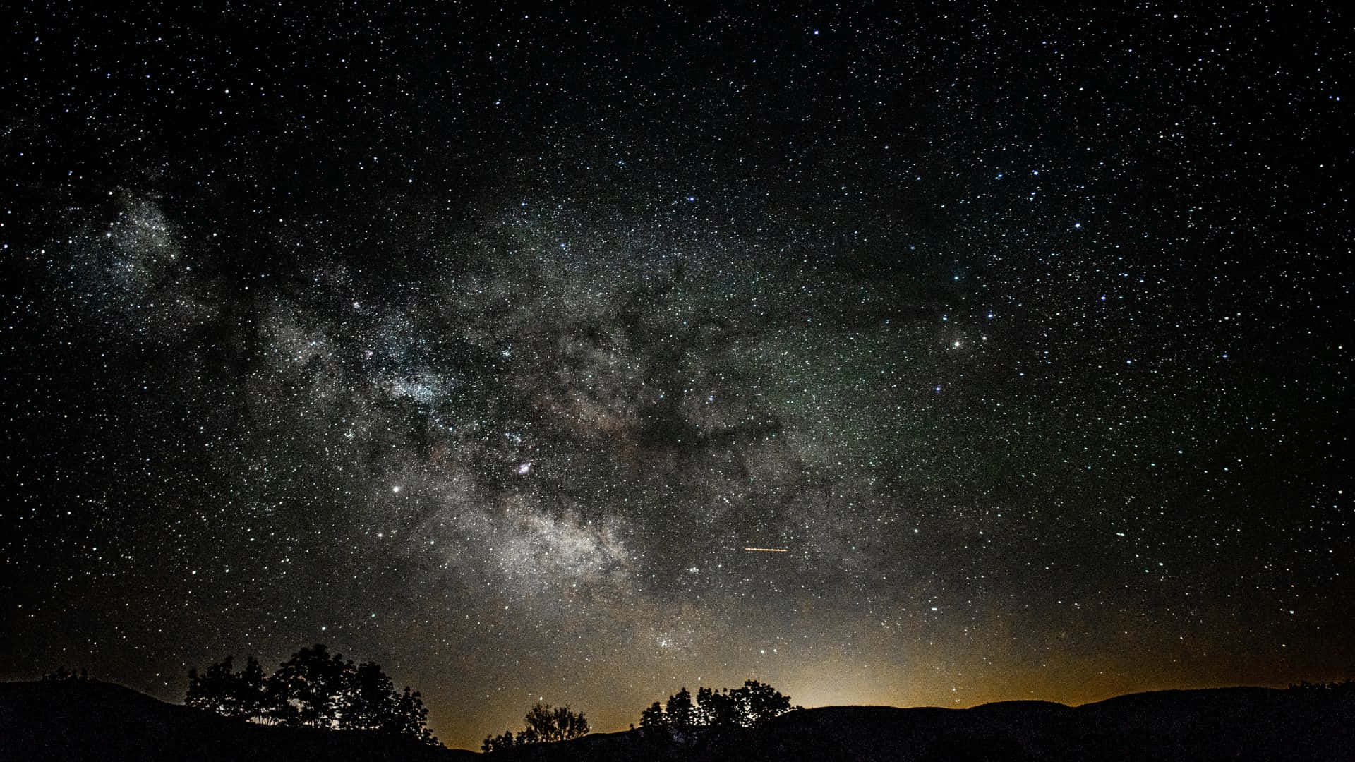 Dark Night 桌布 壁紙 — 一個令人屏息的夜空，充滿無數星星和銀河，拱形跨越黑暗的山脈和樹木剪影。