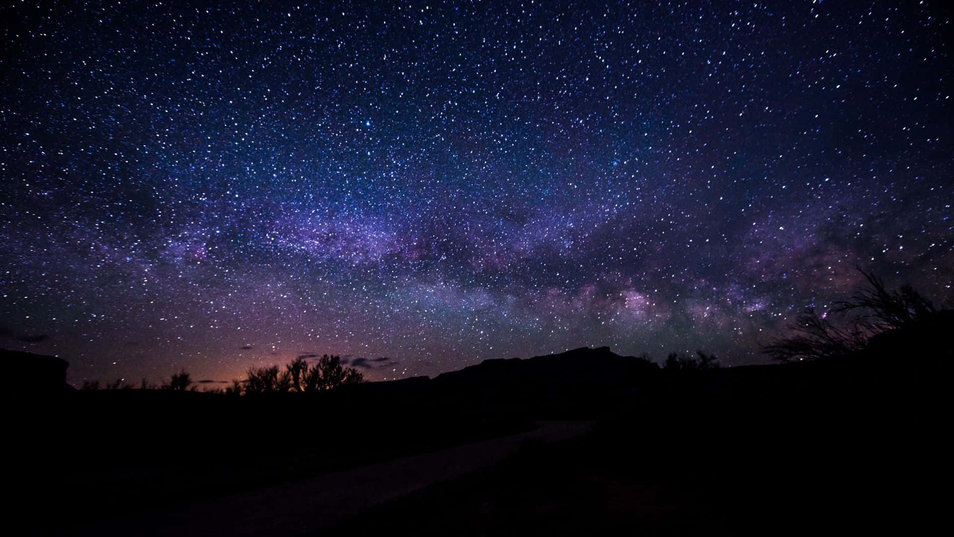 Dark Night 桌布 壁紙 — 一個令人屏息的夜空，充滿無數星星和一條充滿活力的紫色銀河，拱在黑暗的山丘剪影之上。