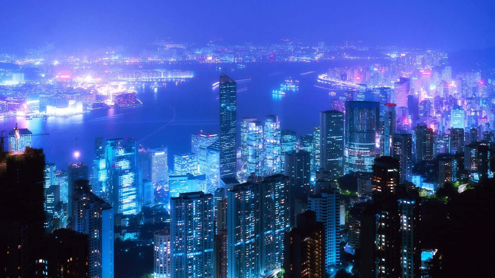 Chilly Night 桌布 壁紙 — 一個令人眼花繚亂的夜景，海濱高聳的摩天大樓閃爍著電光藍和紫色的光芒。