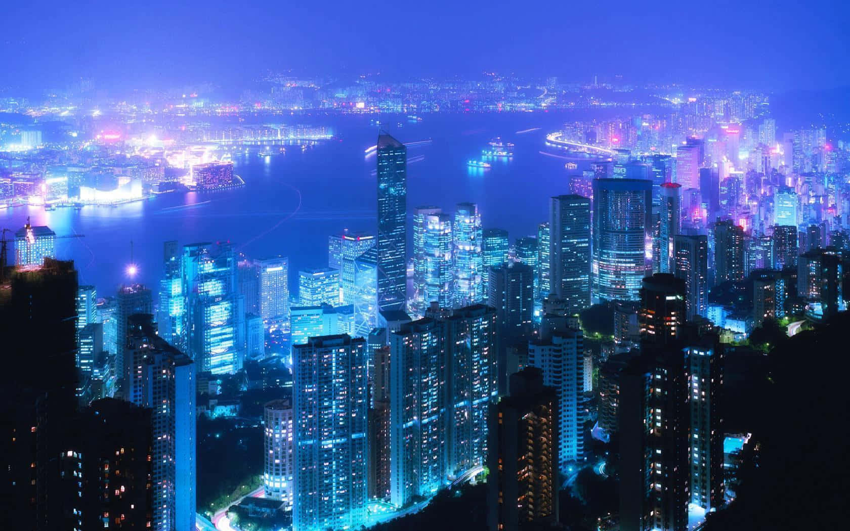 城市景觀 桌布 壁紙 — 一個令人眼花繚亂的夜景城市景觀，高聳的摩天大樓沿著閃閃發光的水濱發出電藍色和紫色的光芒。