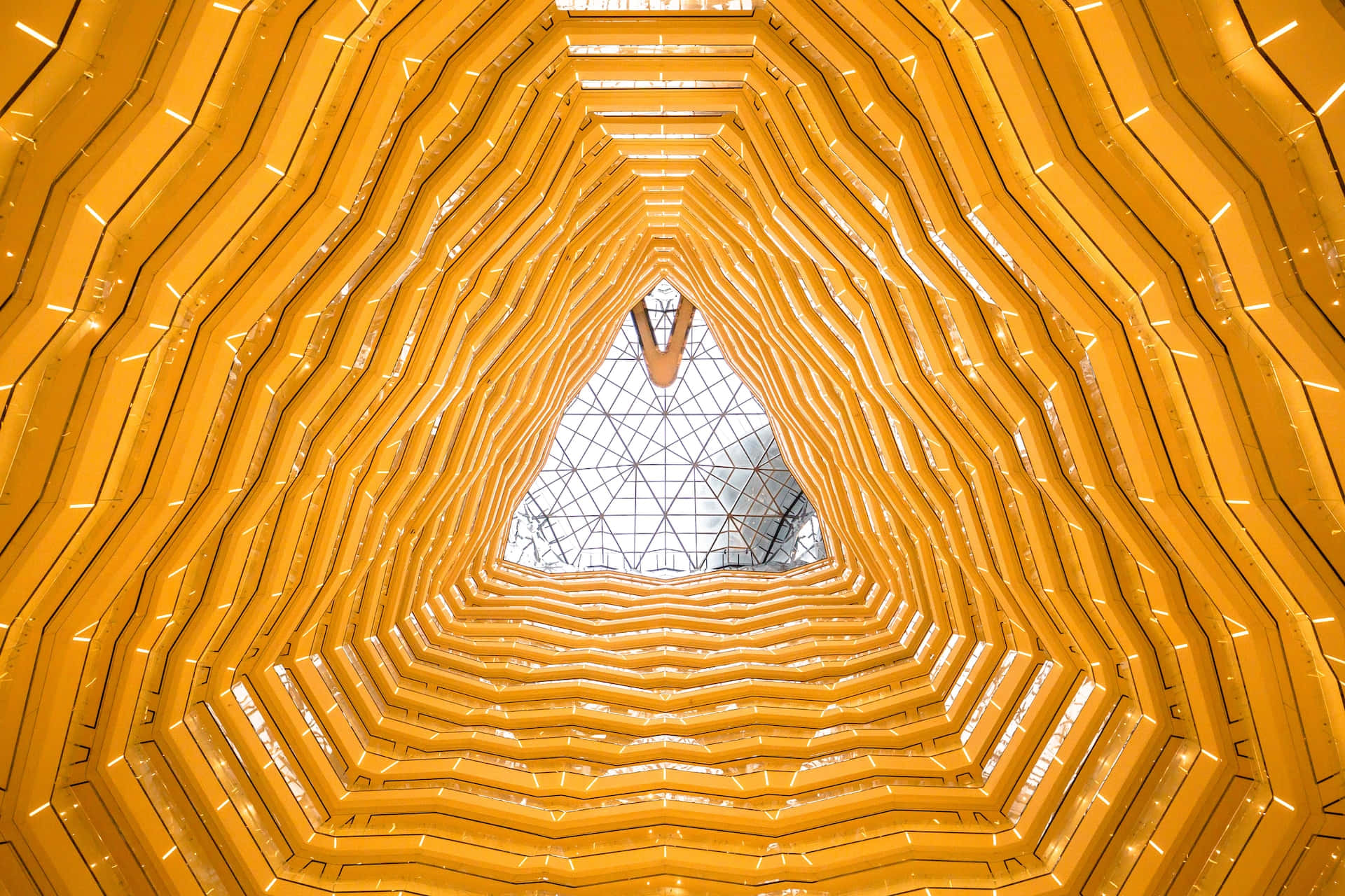 Yellow Pattern 桌布 壁紙 — 一個令人著迷的向上視角，穿過金色波浪形隧道，露出上方幾何玻璃天花。