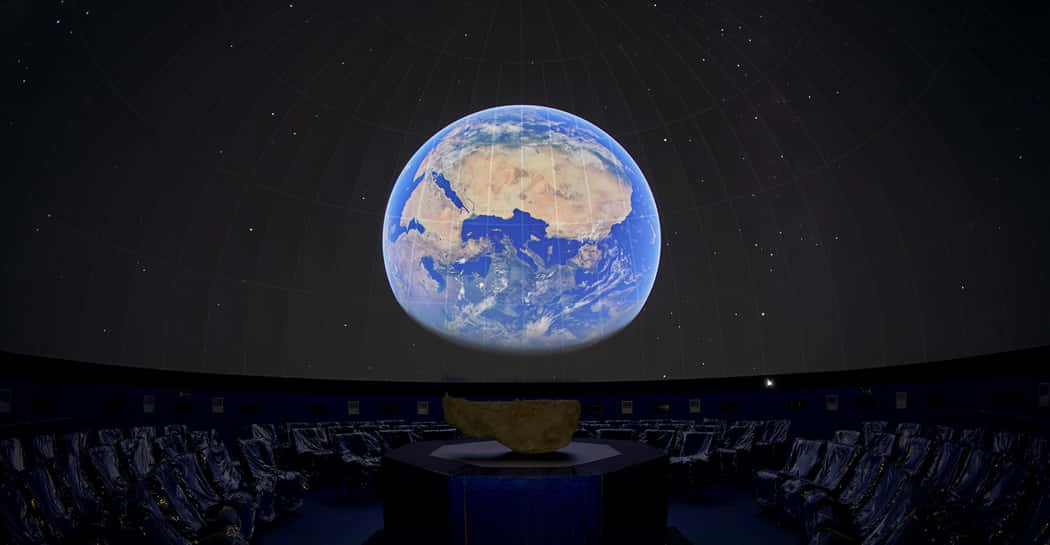 Planetarium 桌布 壁紙 — 一個令人驚嘆的天象館圓頂展示了一個生動的地球懸浮在中央講台上方，下方是一排排空座位。