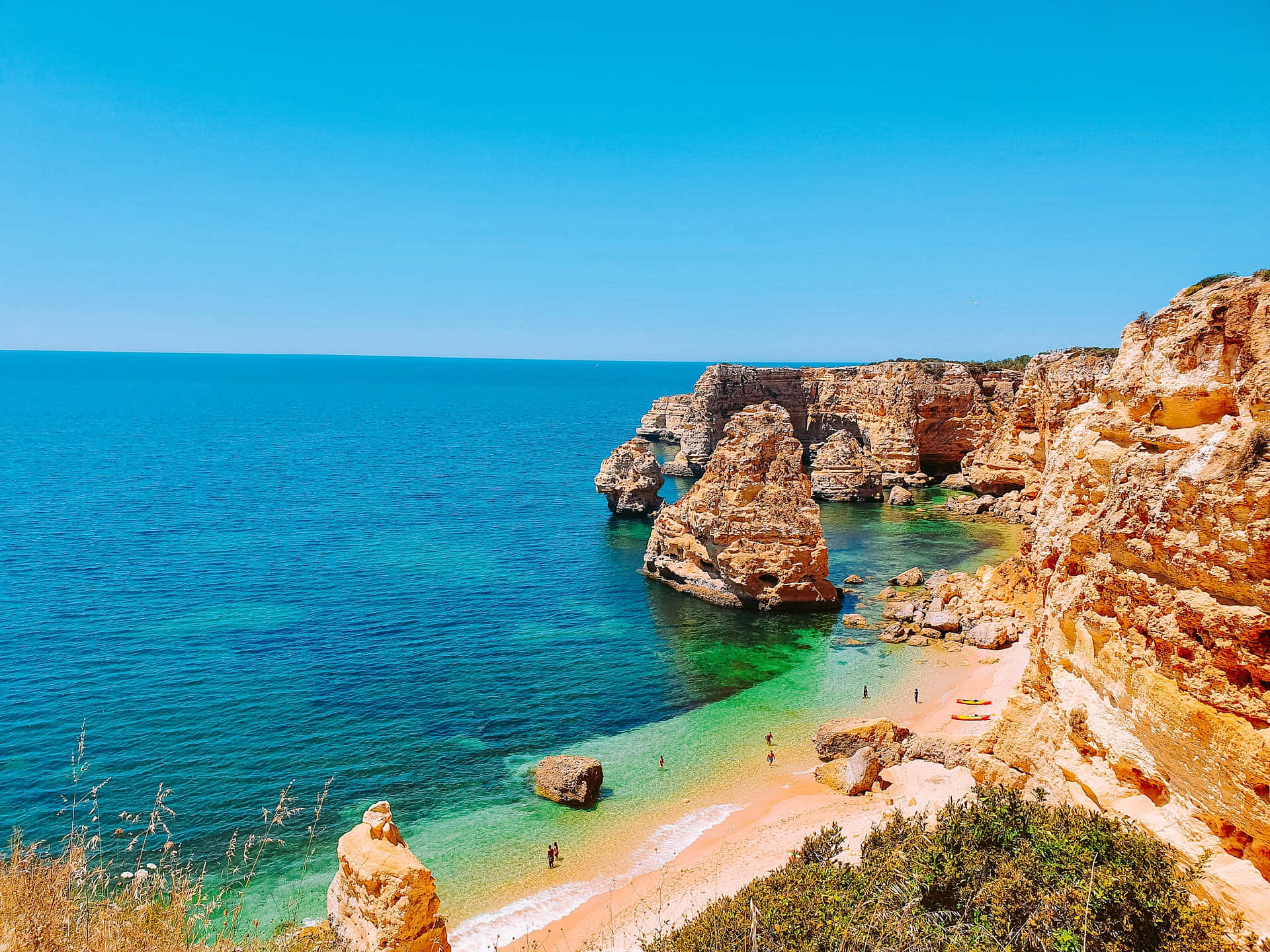 Portuguese Beach 桌布 壁紙 — 一個令人驚嘆的海岸小海灣，碧綠的海水隱藏在金色懸崖之間，上方是清澈的藍天。