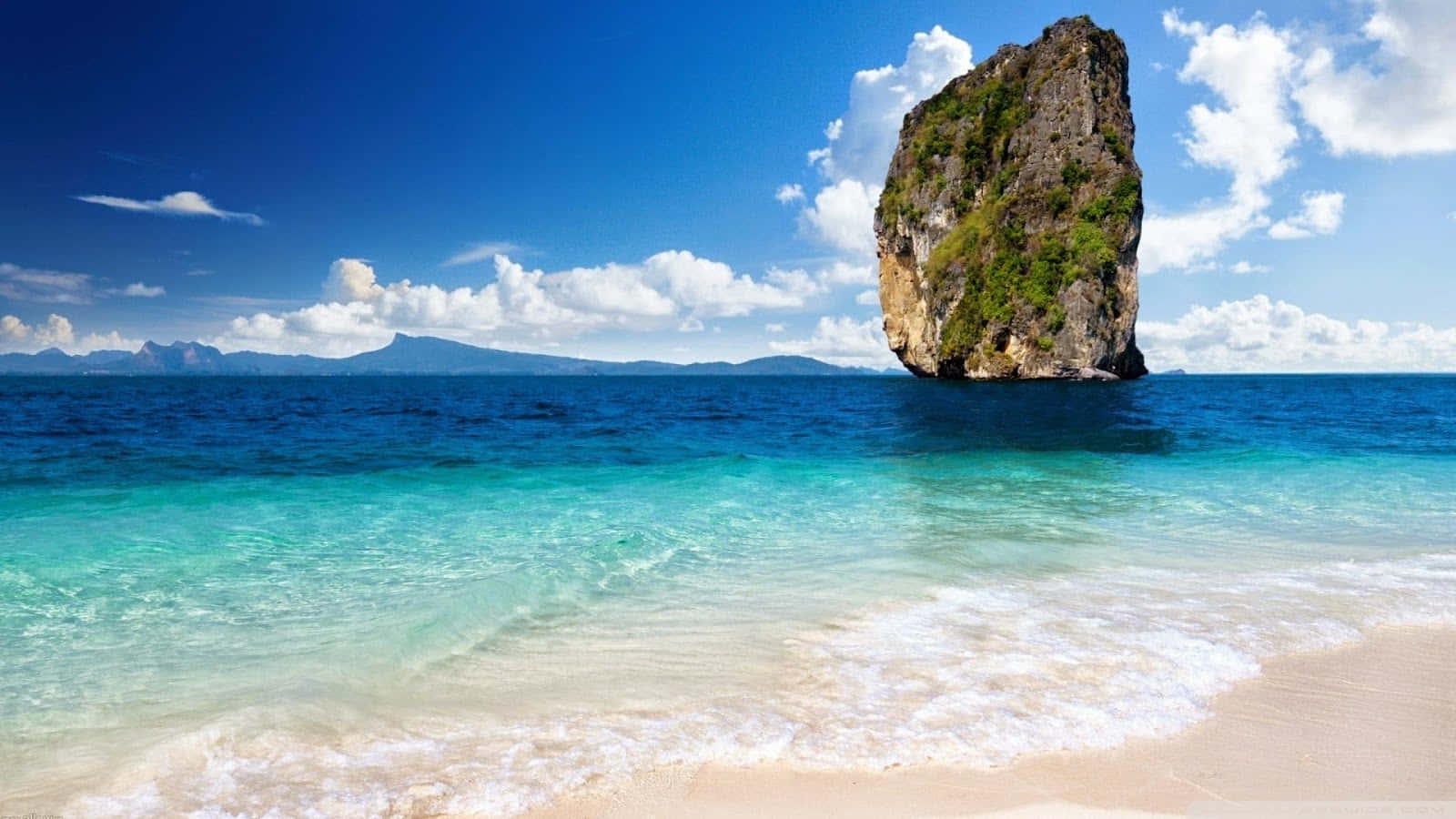 Beach Sand 桌布 壁紙 — 一個令人驚嘆的熱帶海灘，擁有碧綠的海水、溫柔的海浪，以及一座從海中聳立的石灰岩懸崖，在明亮的藍天下。