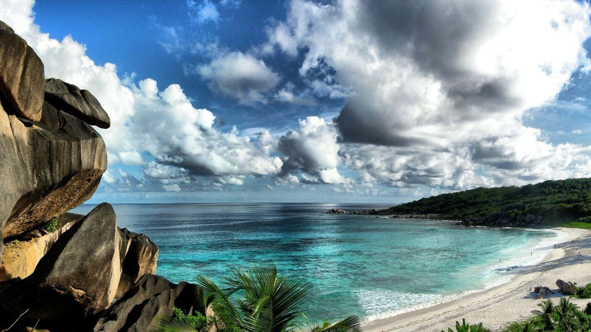 Beautiful Ocean 桌布 壁紙 — 一個令人驚嘆的熱帶海灘，擁有碧綠的海水、白色沙灘和巨大的花崗岩巨石，在戲劇性的多雲天空下。