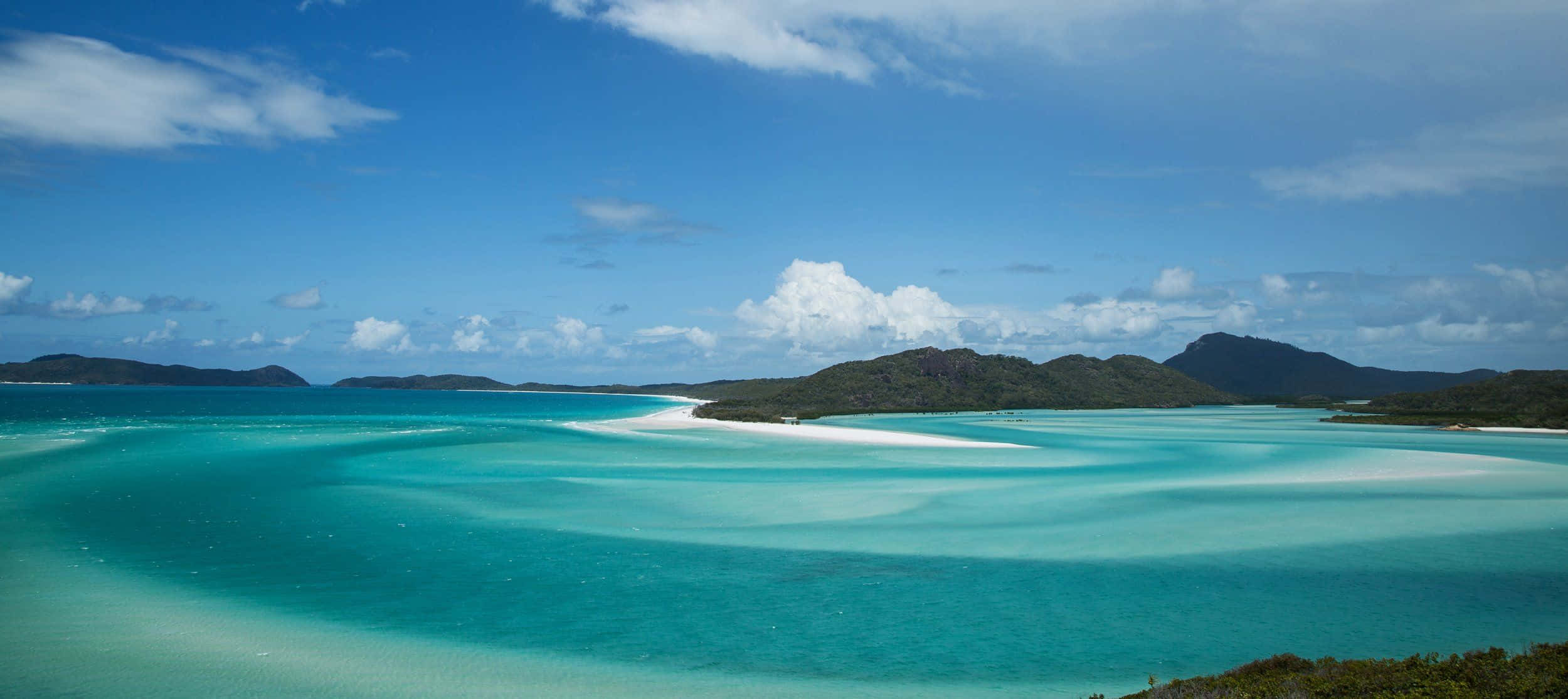 Australia Beach 桌布 壁紙 — 一個令人驚嘆的熱帶潟湖，擁有碧綠的海水和白色的沙洲曲線，在明亮的藍天和散落的雲朵下。