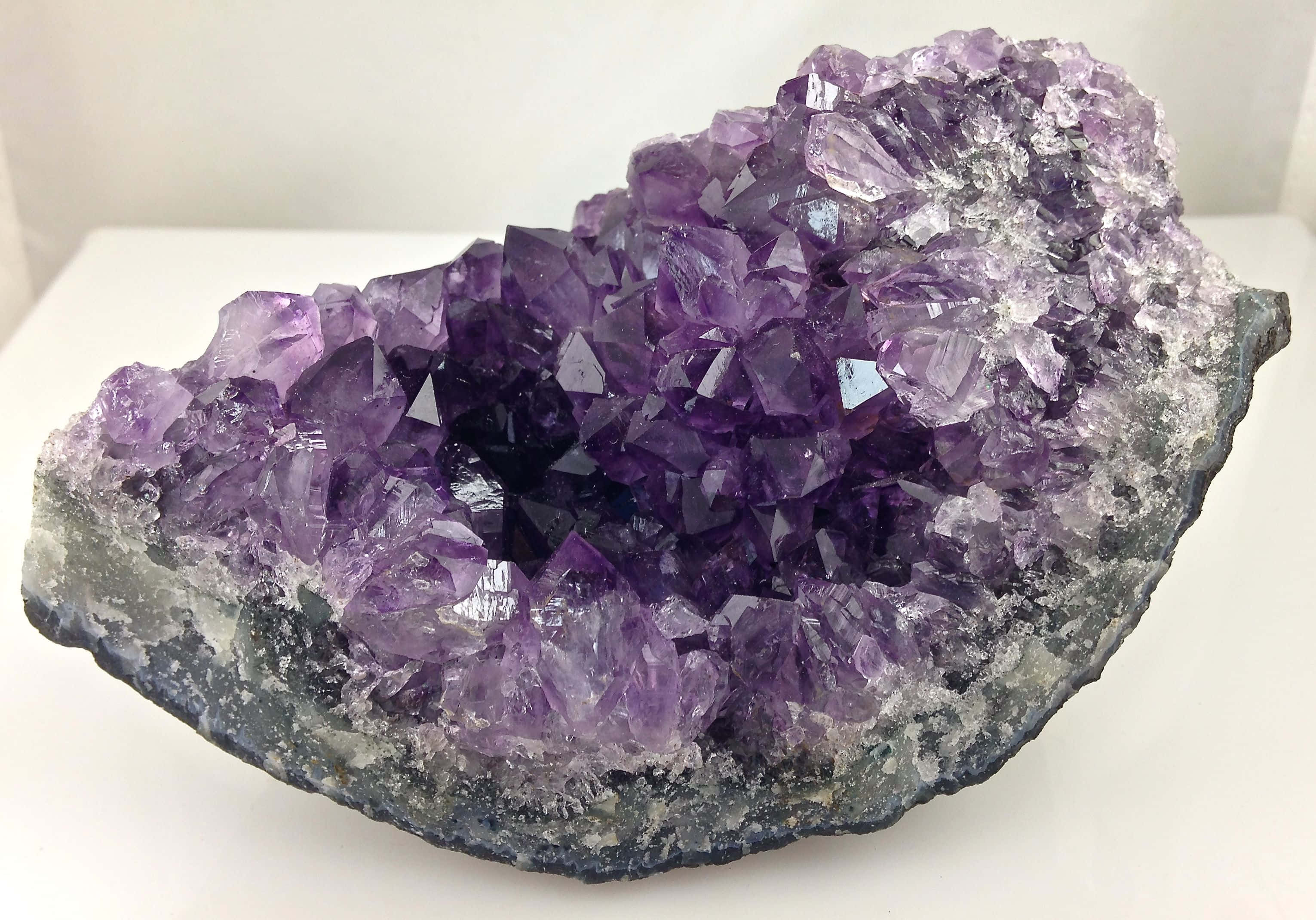 Amethyst 桌布 壁紙 — 一個令人驚嘆的紫水晶晶洞，深紫色晶體在柔和光線下閃耀，背景為潔淨的白色。