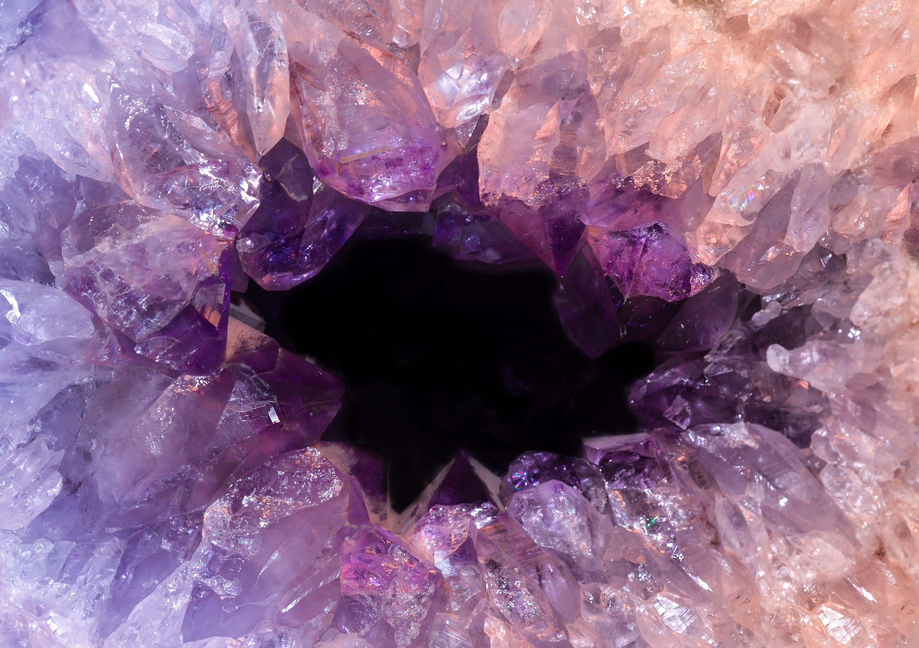 Amethyst 桌布 壁紙 — 一個令人驚嘆的紫水晶洞的近距離視圖，閃閃發光的紫色水晶環繞著一個黑暗的空心中心。