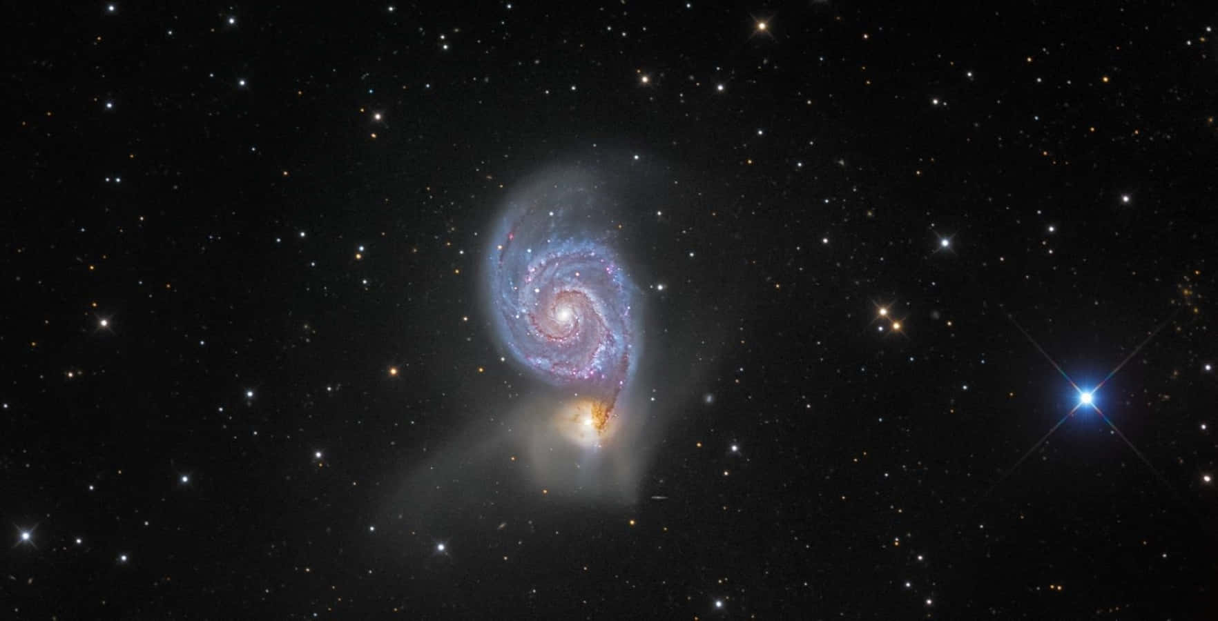 Whirlpool Galaxy 桌布 壁紙 — 一個令人驚嘆的螺旋星系，帶有藍色和紫色的旋臂，在點綴著明亮恆星和一個顯著藍色星爆的星場中旋轉。