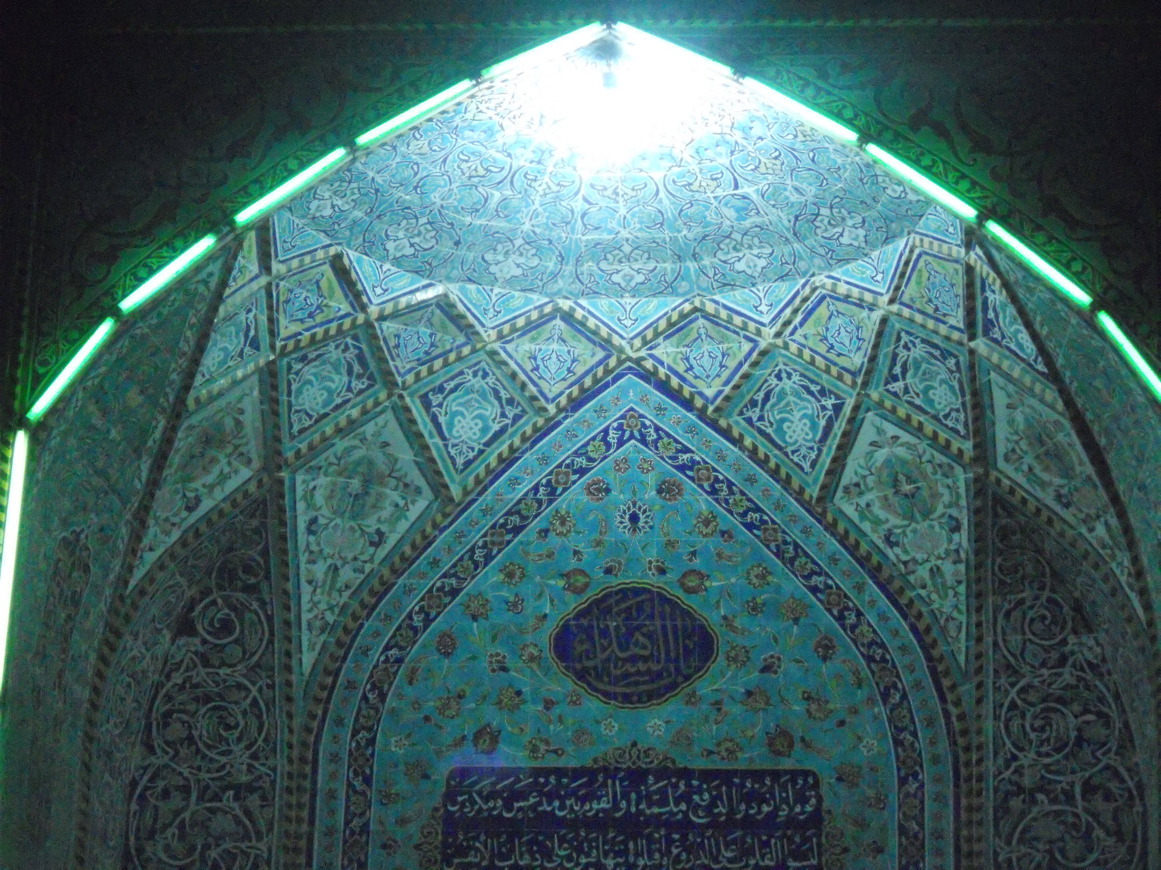 Karbala 桌布 壁紙 — 一個令人驚嘆的複雜藍綠瓷磚圓頂，發光的霓虹燈照亮了華麗的伊斯蘭書法和幾何圖案。