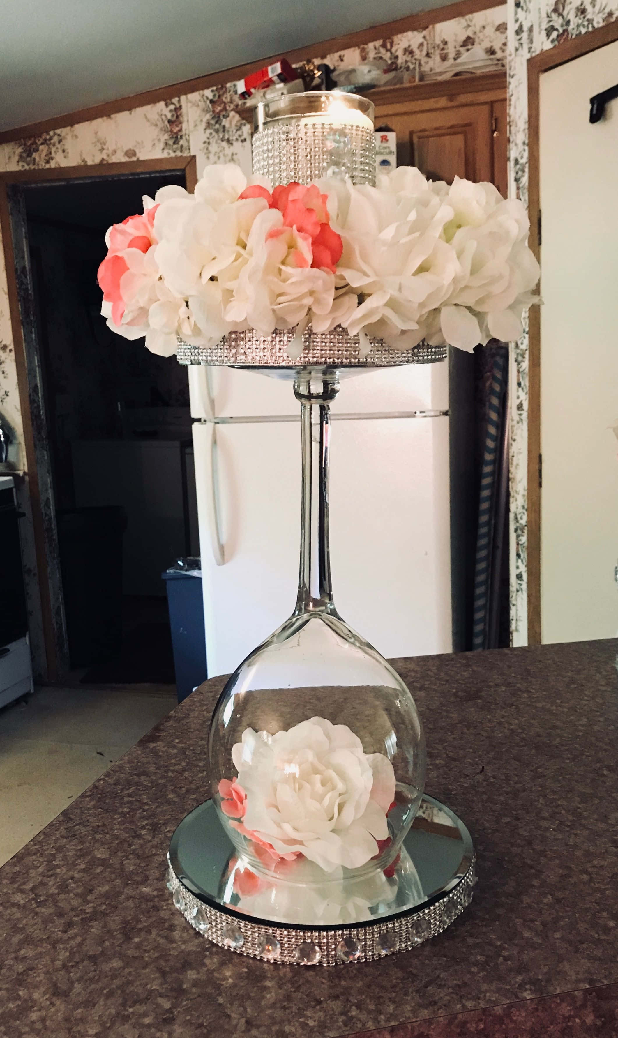 Centerpiece 桌布 壁紙 — 一個以白色和珊瑚色花朵裝飾的酒杯中心裝飾，放置在廚房斑點檯面上的鏡面底座上。