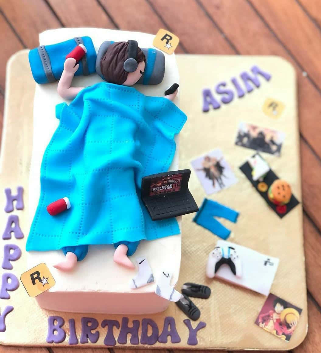 Cake Fondant 桌布 壁紙 — 一個以遊戲玩家為造型的生日蛋糕，躺在床上，周圍有耳機、手提電腦、控制器和動漫照片。