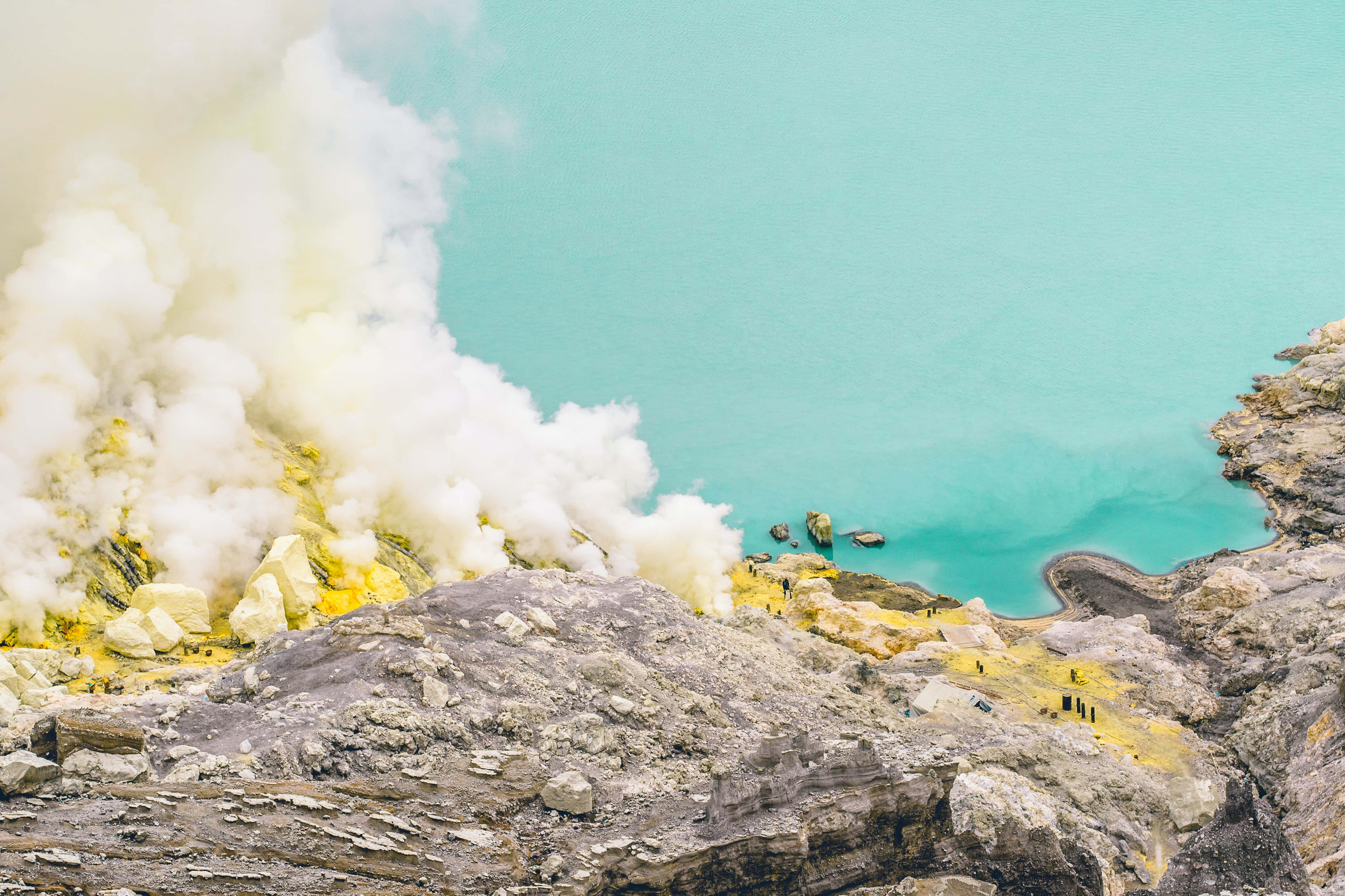 Mining 桌布 壁紙 — 一個位於火山口內的鮮豔藍綠色湖泊，富含硫磺的黃色岩石上蒸氣裊裊升起。