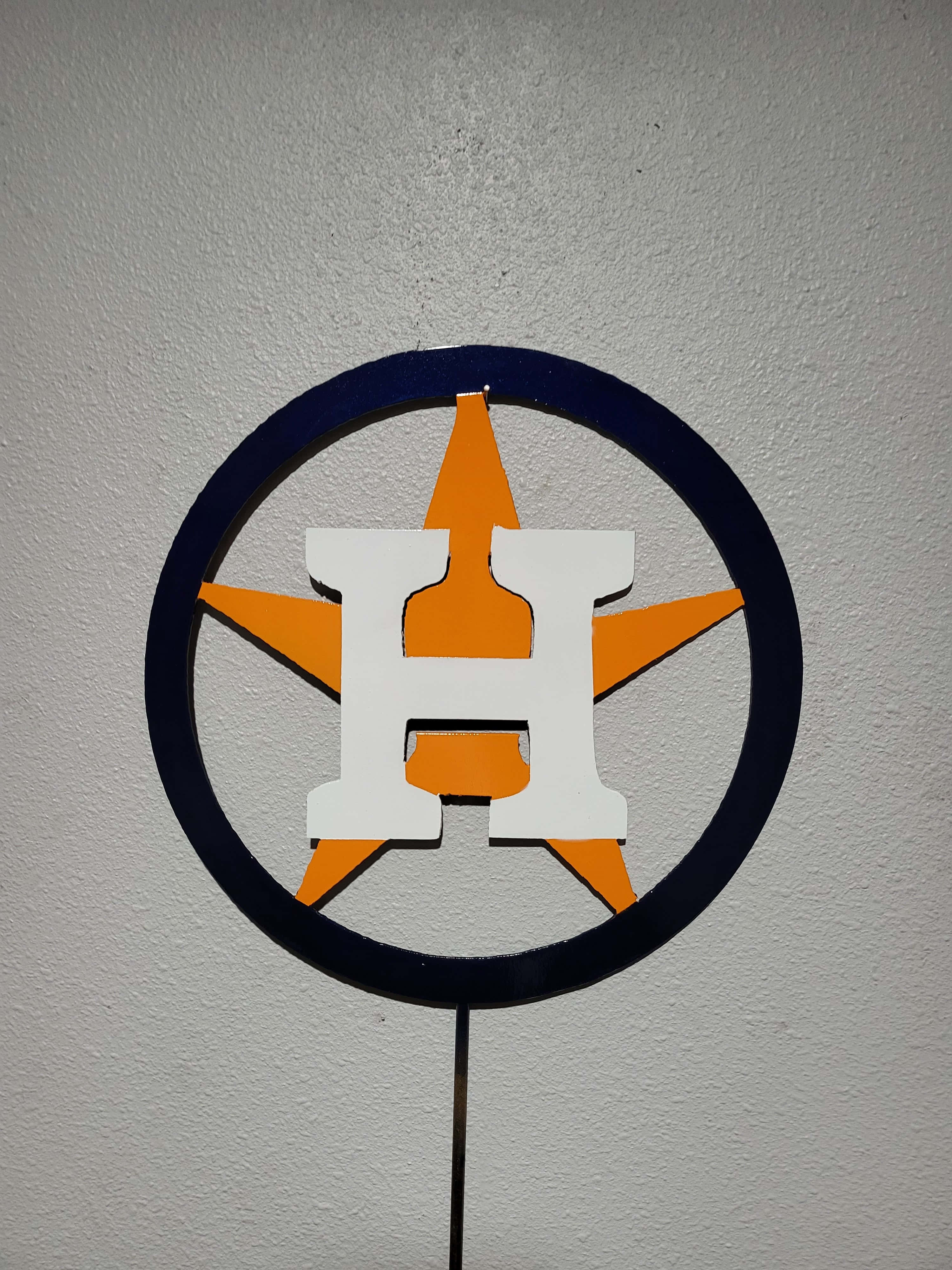 Astros 桌布 壁紙 — 一個侯斯頓太空人標誌剪影，白色H、橙色星同海軍藍圓圈，安裝喺有紋理嘅牆上。