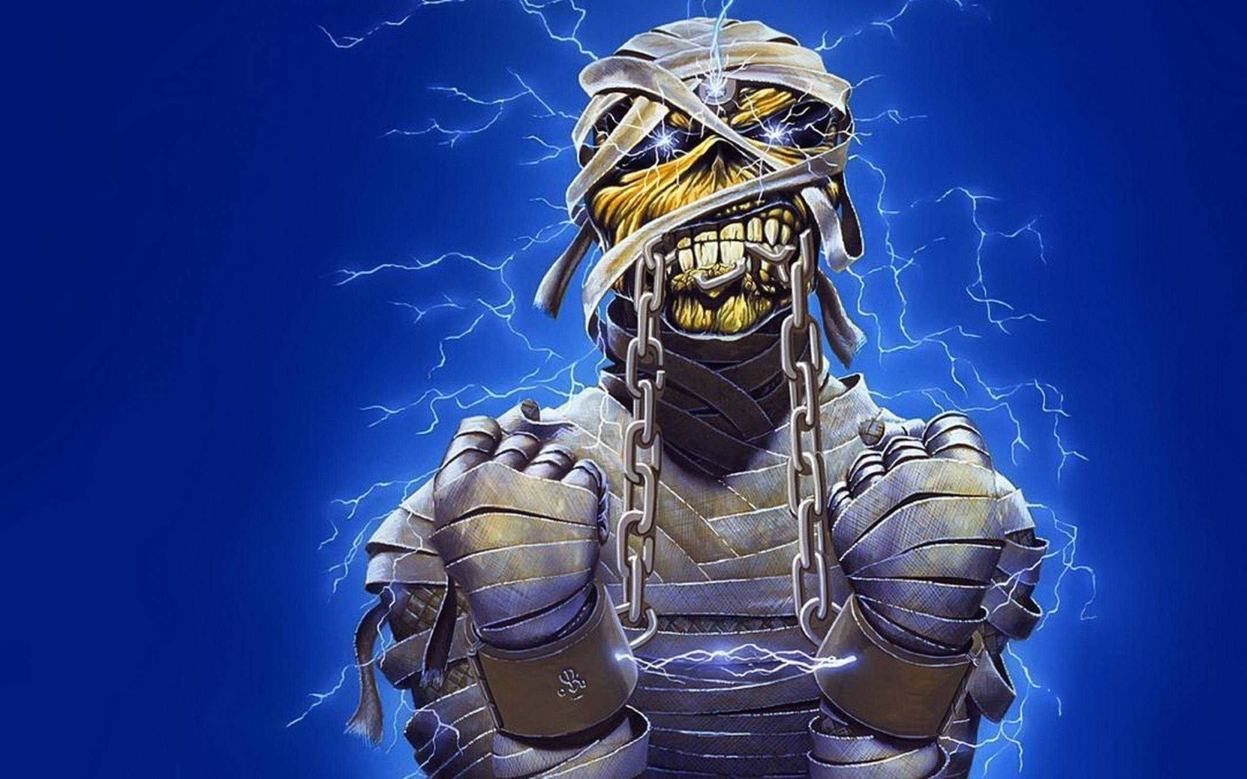Iron Maiden Eddie In Chains 壁紙 — 一個像木乃伊的頭骨，帶有金牙和鎖鏈，背景是深藍色，閃電劈啪作響。