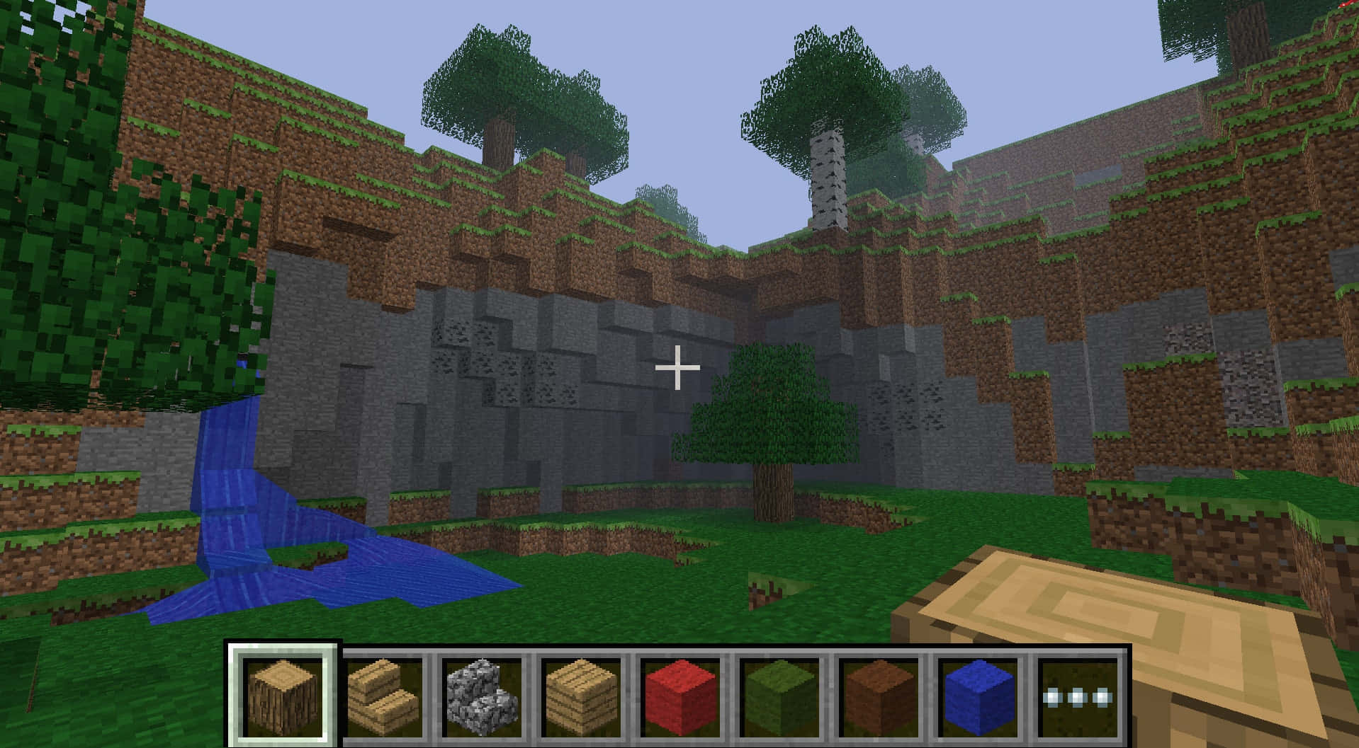Minecraft Pocket Edition 桌布 壁紙 — 一個像素化的Minecraft景觀，瀑布流入一個被方塊樹木和石崖環繞的草地山谷。