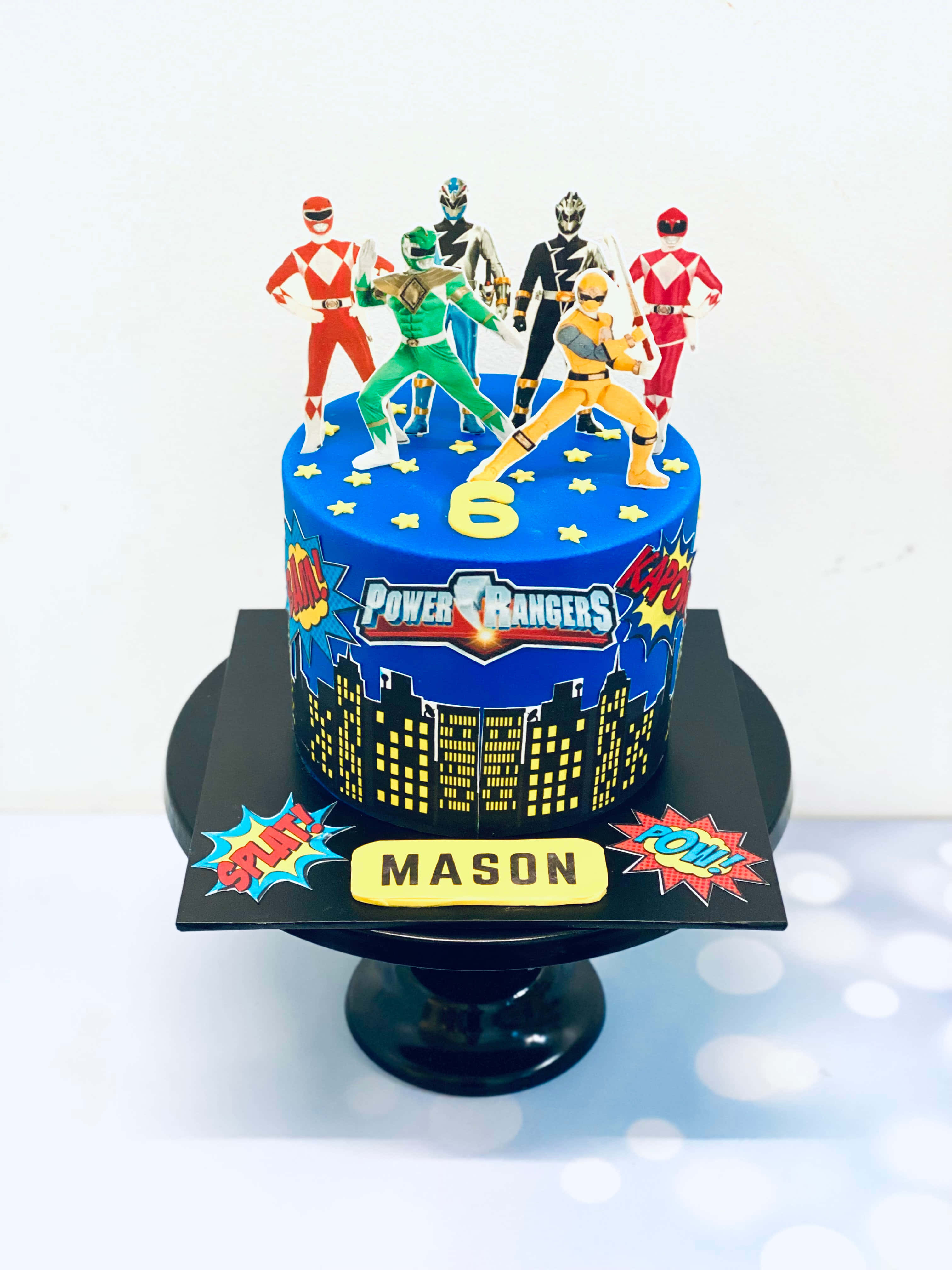 Cake Fondant 桌布 壁紙 — 一個充滿活力的Power Rangers主題生日蛋糕，上面有五個公仔，藍色星星設計和城市景觀底座。
