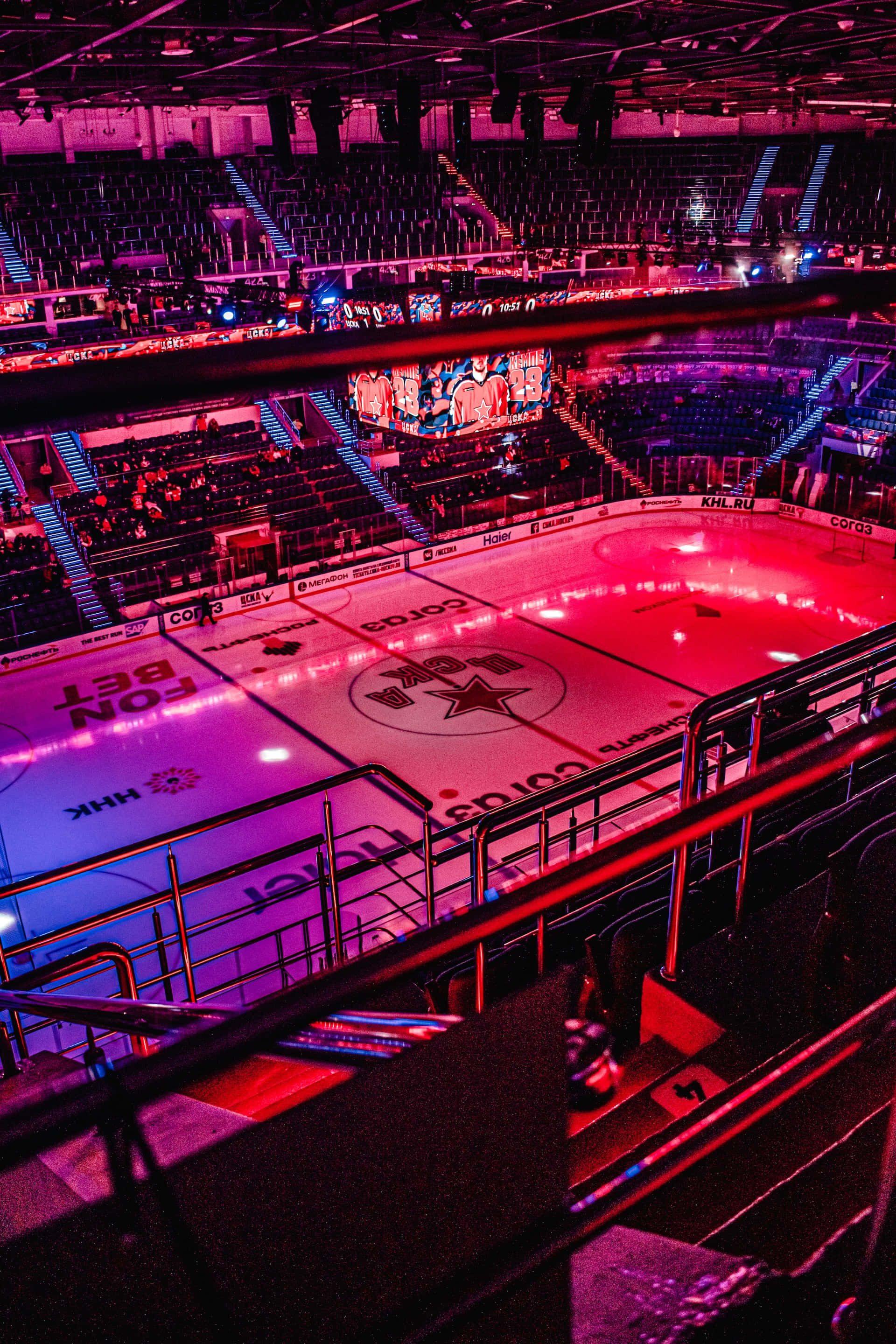 Ice Rink 桌布 壁紙 — 一個充滿活力的冰球場，在黑暗的競技場和空座位下，沐浴在電光粉紅和藍色燈光中。