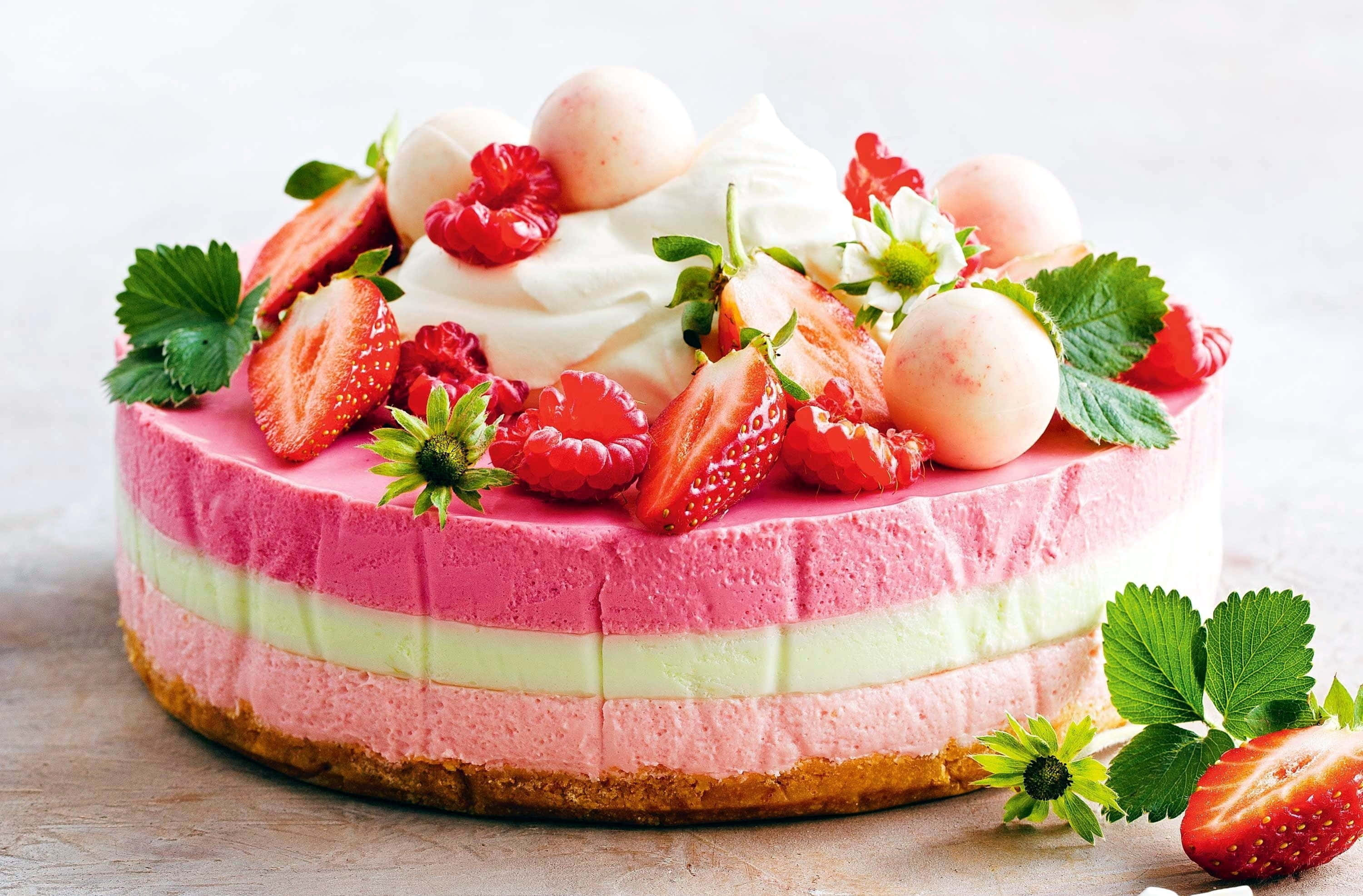 Spring Desserts 桌布 壁紙 — 一個充滿活力的分層草莓芝士蛋糕，上面鋪滿新鮮莓果、忌廉和綠葉，放在木質表面上。