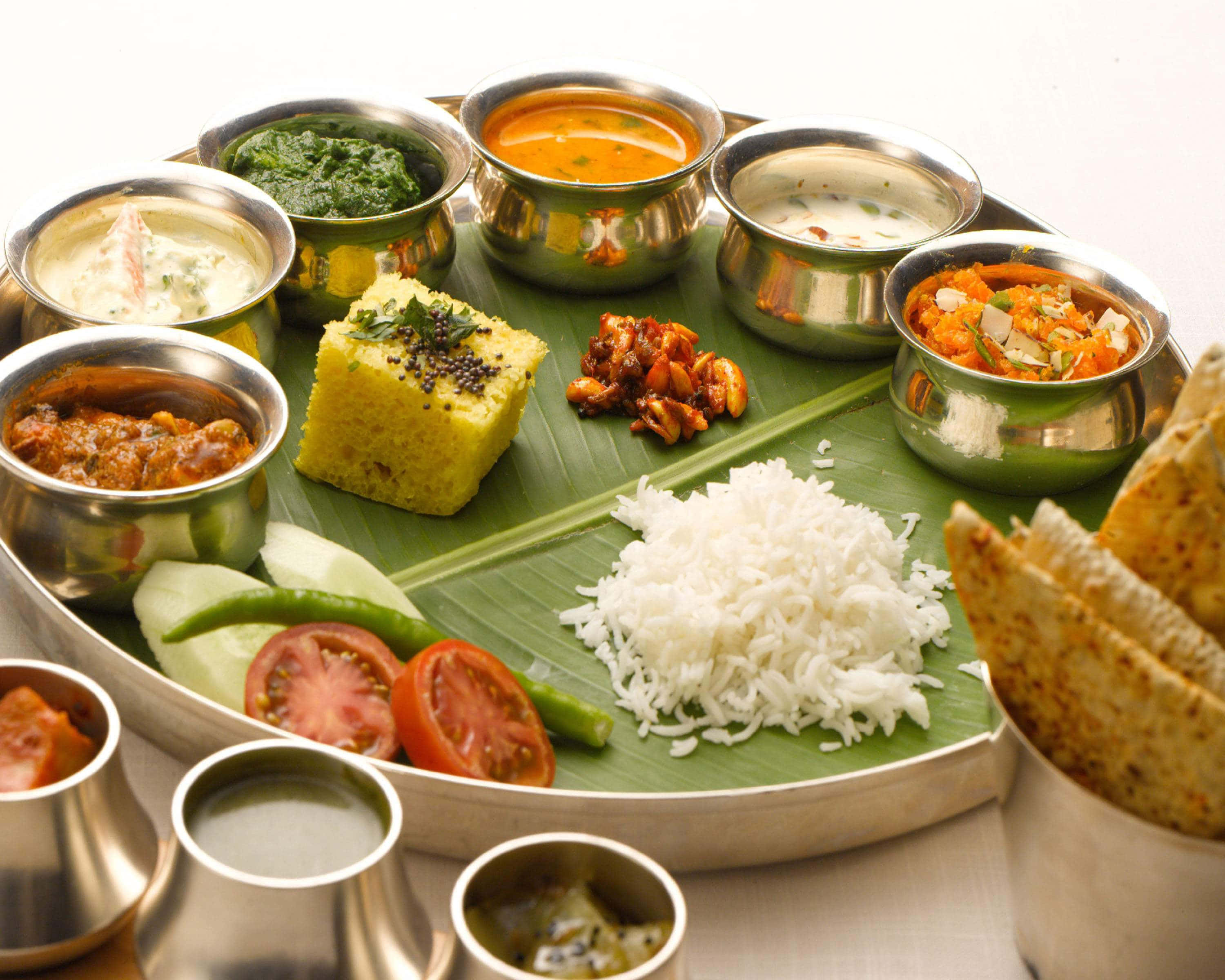 Thali 桌布 壁紙 — 一個充滿活力的印度塔利，盛載在香蕉葉上，配有米飯、桑巴爾豆湯和各種咖哩，放在閃亮的金屬碗中。