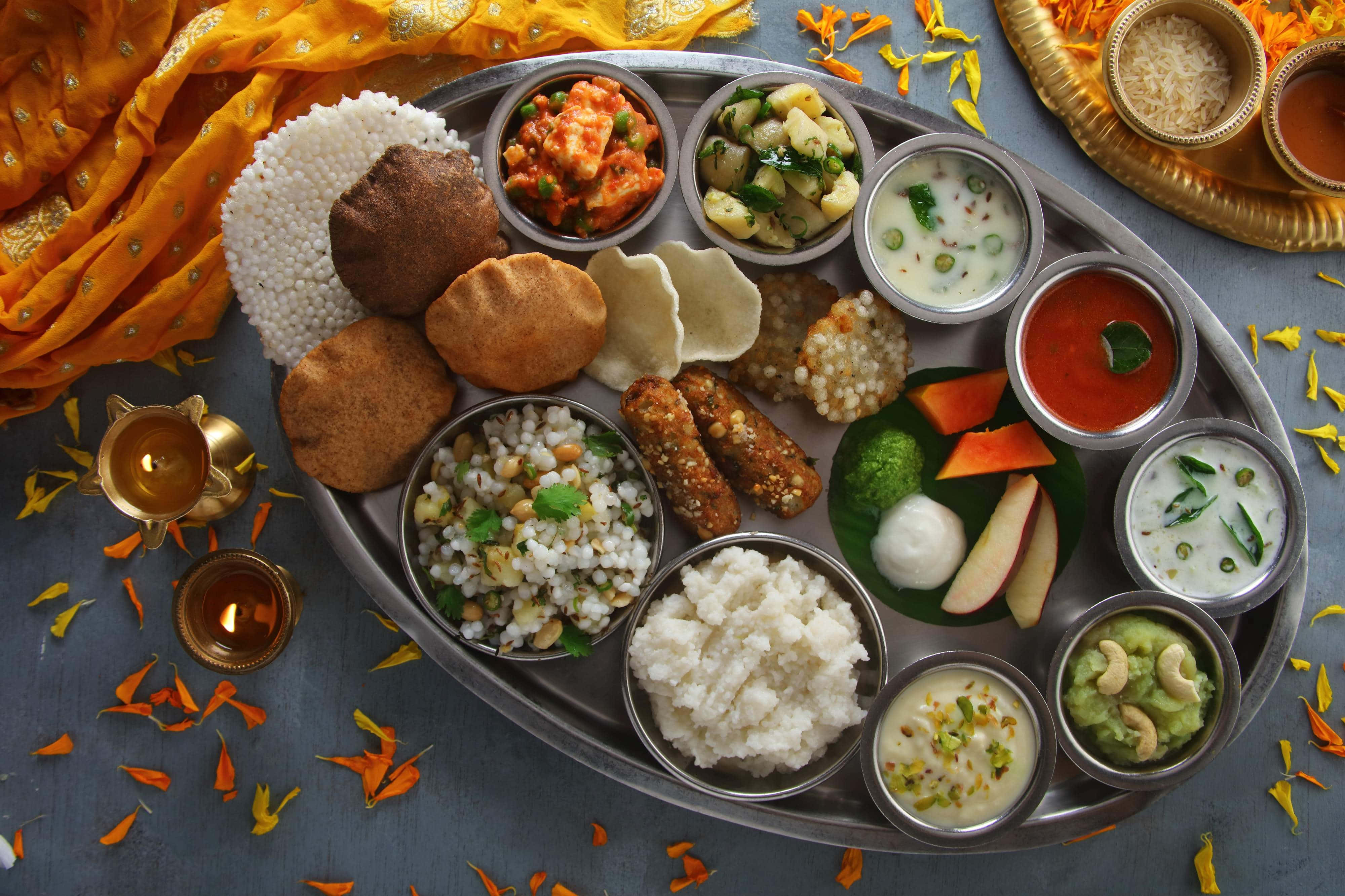 Thali 桌布 壁紙 — 一個充滿活力的印度塔利，銀托盤上的金屬碗裡盛放著各式菜餚，周圍環繞著萬壽菊花瓣和點燃的油燈。