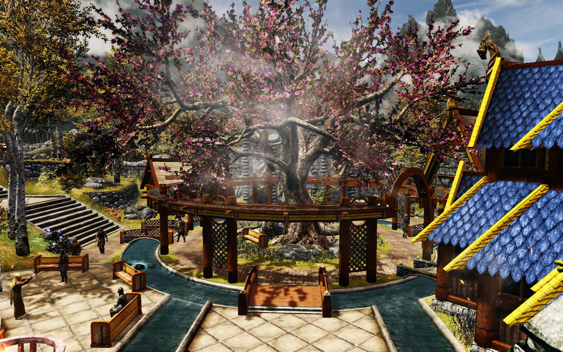 Skyrim Whiterun 桌布 壁紙 — 一個充滿活力的奇幻村莊中心，有一棵盛開粉紅色花朵的巨大樹木，周圍環繞著木造建築和石頭小徑，天空多雲。