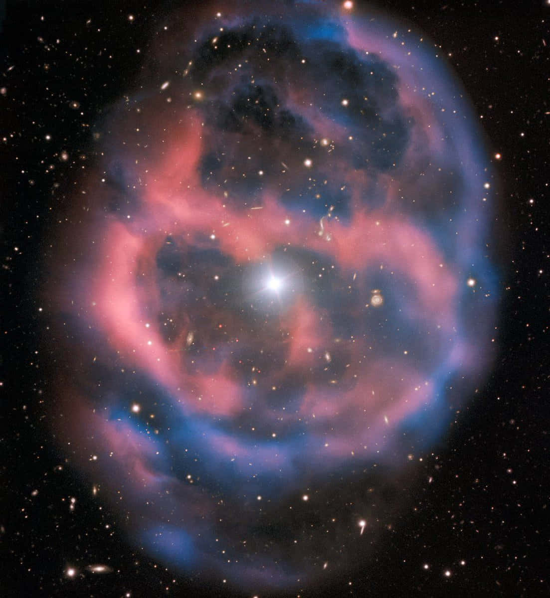 Planetary Nebula 桌布 壁紙 — 一個充滿活力的宇宙星雲，在佈滿星星的黑色虛空中，以鮮豔的粉紅色和藍色旋轉。