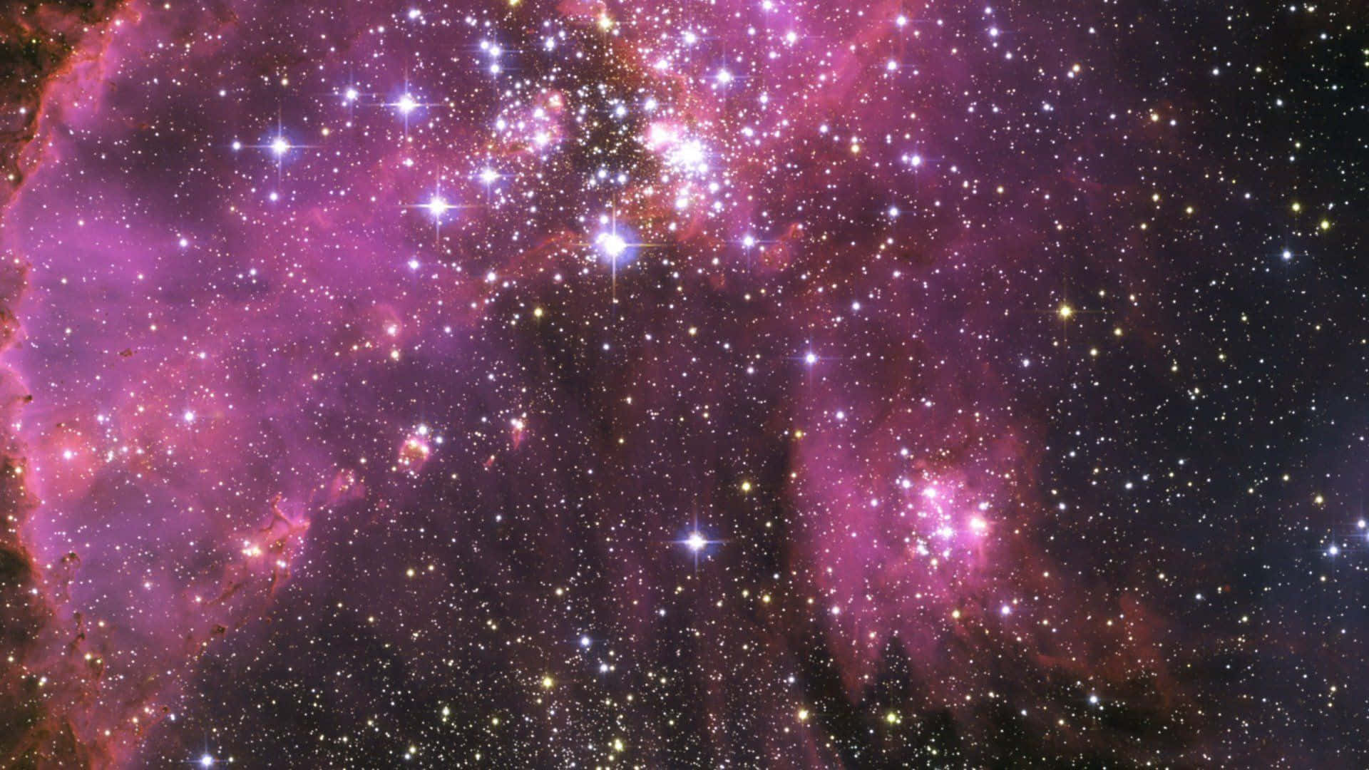 Purple Galaxy 桌布 壁紙 — 一個充滿活力的宇宙星雲，在黑暗虛空中閃耀著粉紅色和紫色調，點綴著無數閃爍的星星。