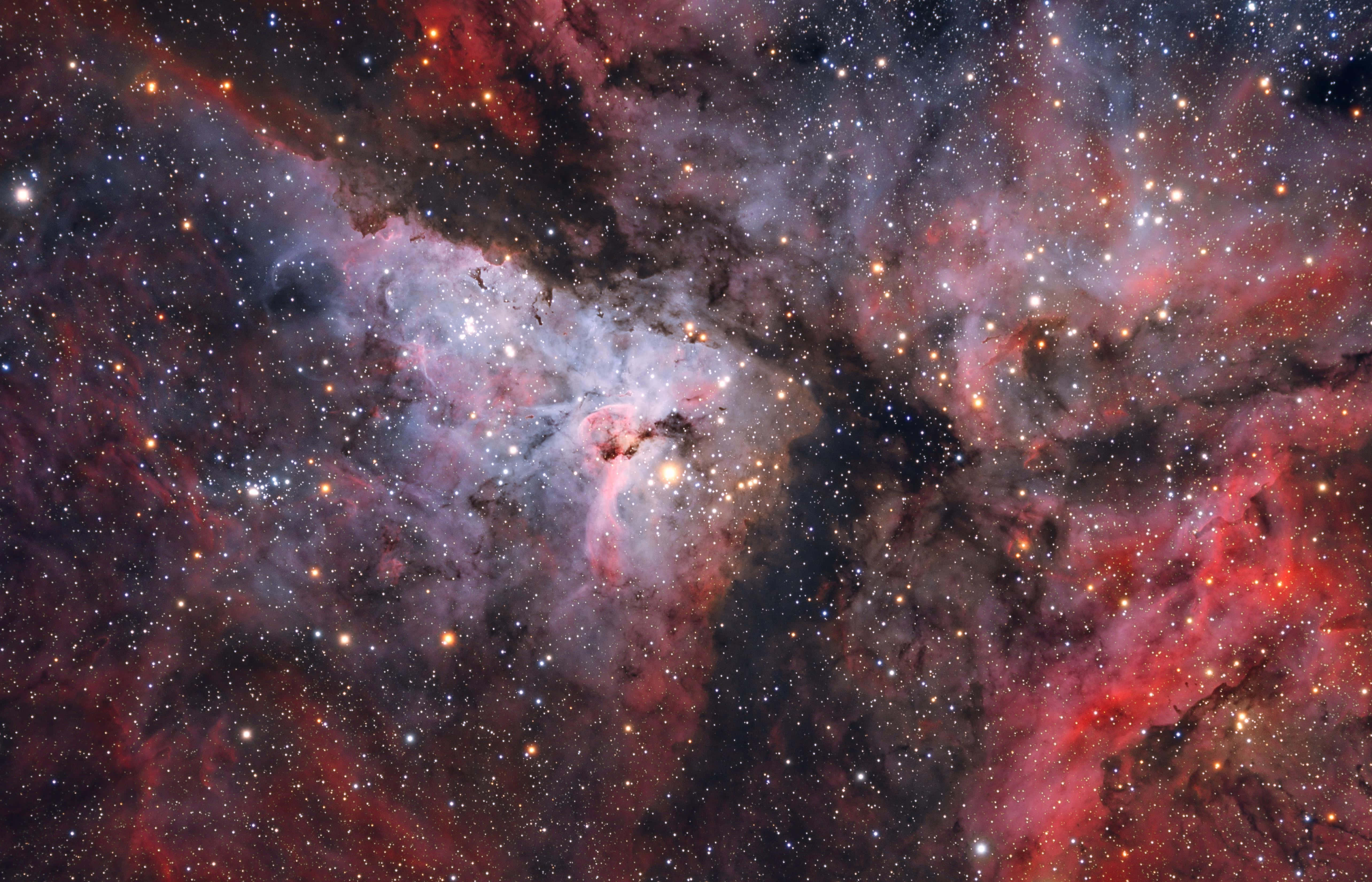 Carina Nebula 桌布 壁紙 — 一個充滿活力的宇宙星雲，由紅色、粉紅色和藍色氣體旋轉而成，在黑暗虛空中被無數閃爍的星星照亮。