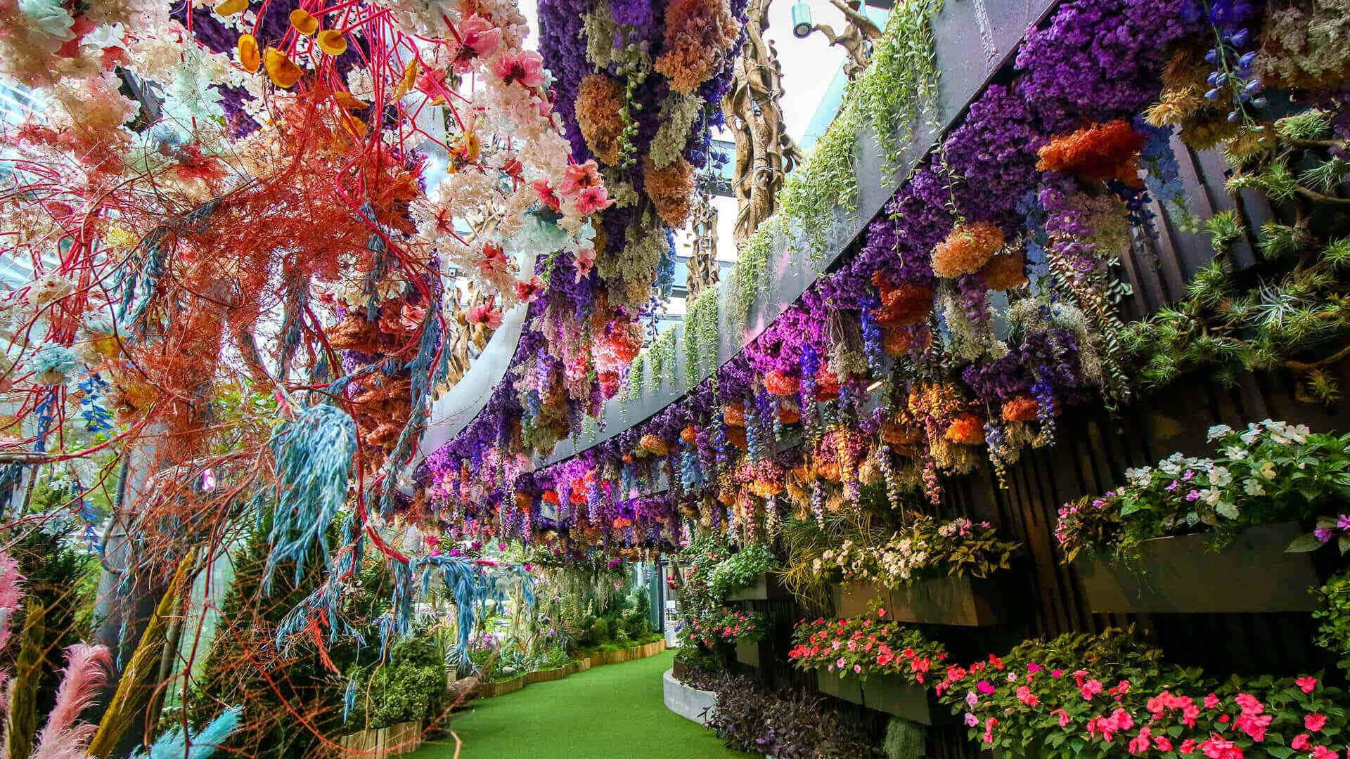 Botanical Garden 桌布 壁紙 — 一個充滿活力的室內花園，在玻璃天花下，色彩繽紛的花朵和樹葉如瀑布般沿著綠色小徑排列。