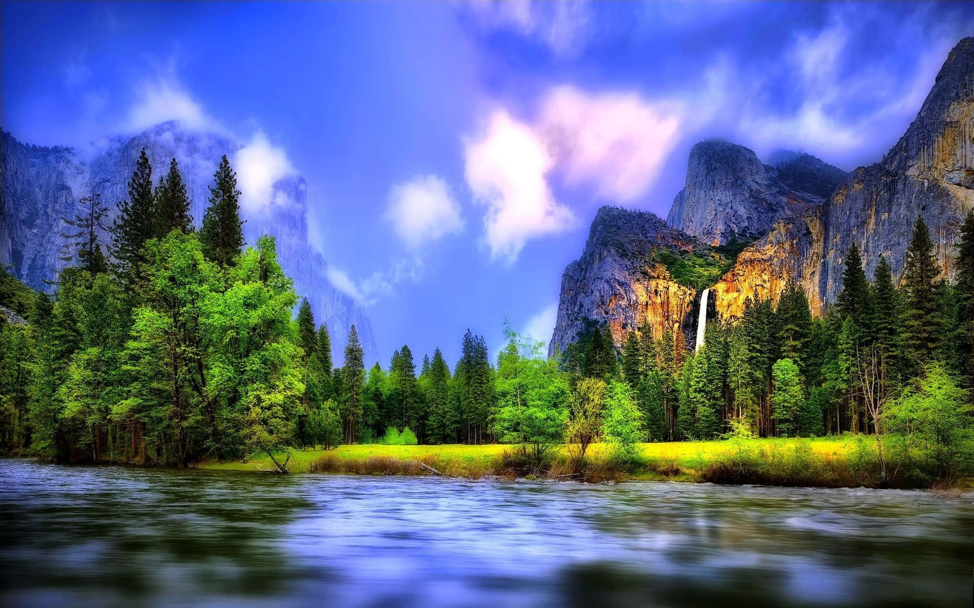 Beautiful Landscape 桌布 壁紙 — 一個充滿活力的山谷，河流流經茂密的綠樹和高聳的懸崖，在戲劇性的藍天下，瀑布從岩壁上傾瀉而下。