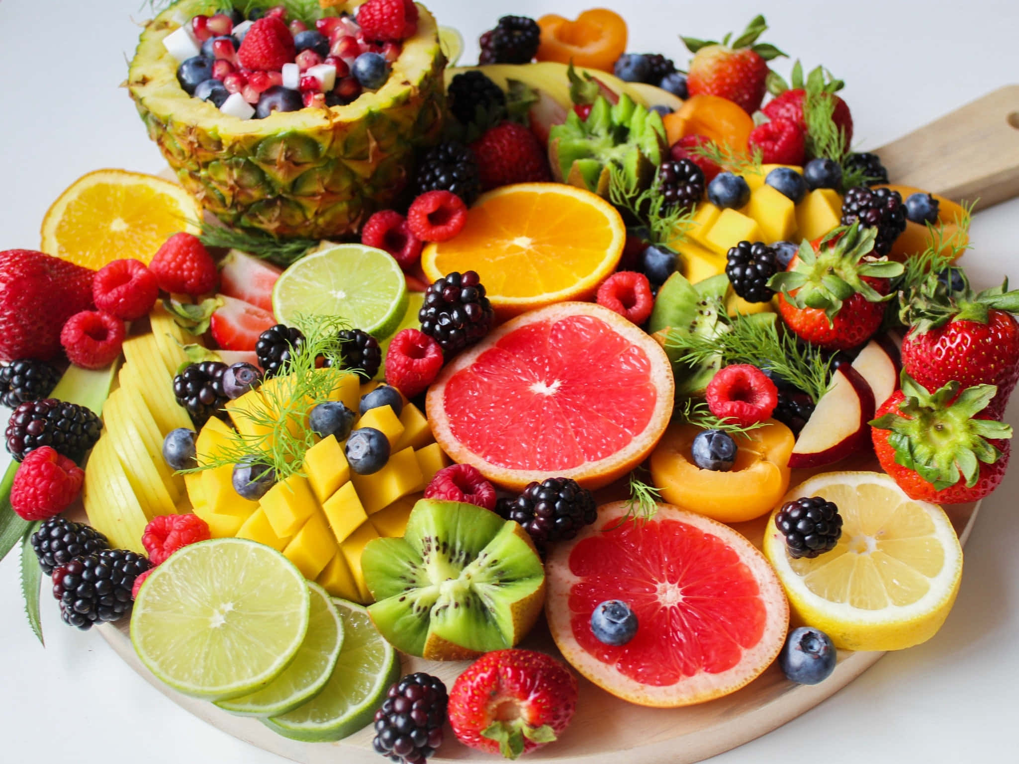Summer Fruits 桌布 壁紙 — 一個充滿活力的拼盤，上面擺滿了色彩繽紛的切片水果，如菠蘿、西柚和草莓，整齊地排列在木板上。