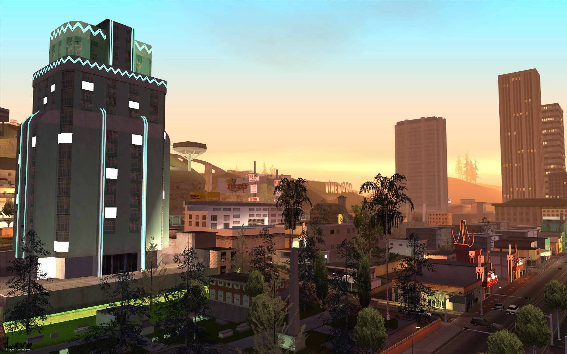 Gta 桌布 壁紙 — 一個充滿活力的日落照耀著一個風格化的城市景觀，特色是霓虹燈閃爍的摩天大樓、棕櫚樹和遠處帶有標誌性荷里活標誌的山丘。