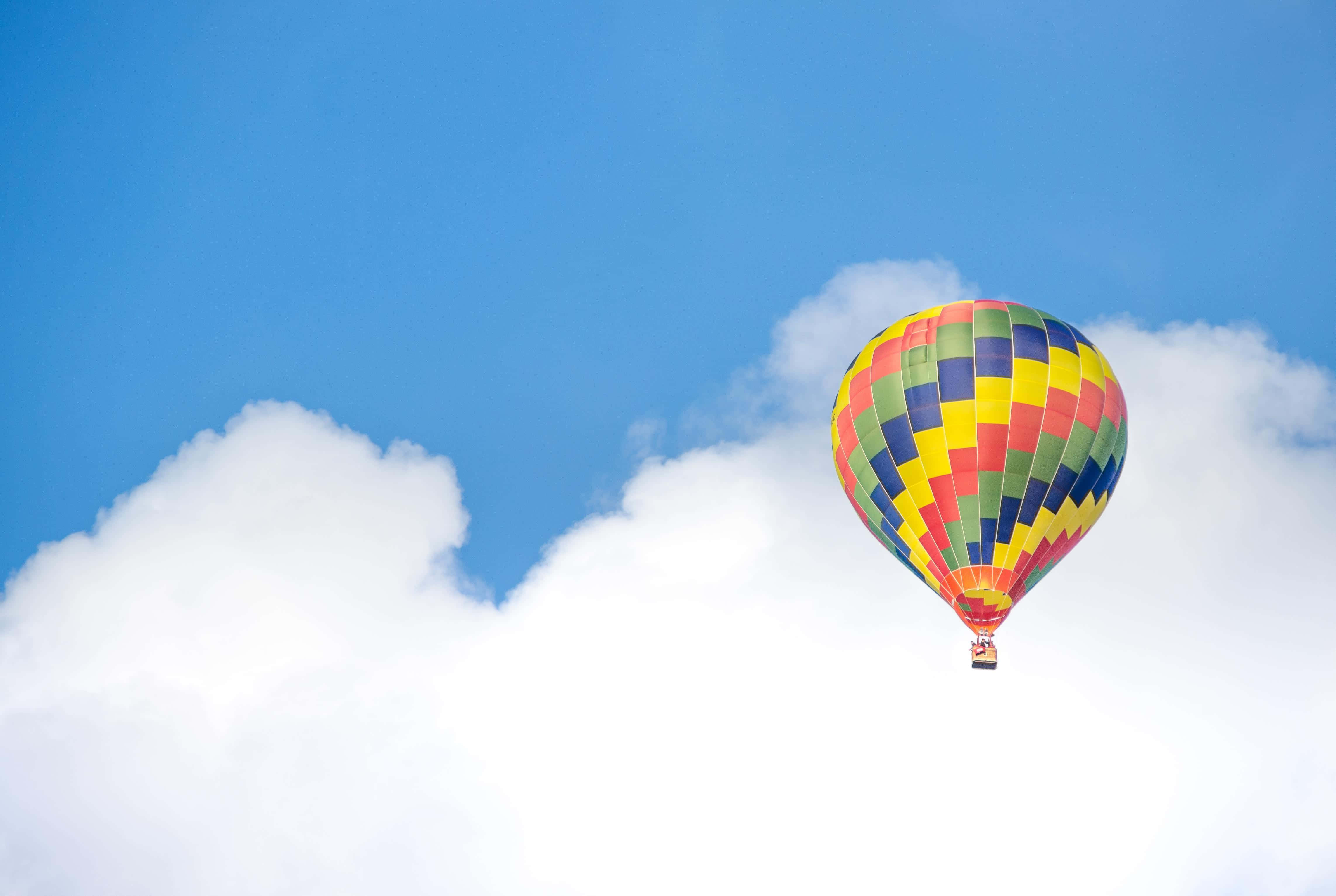 Balloon 桌布 壁紙 — 一個充滿活力的格紋熱氣球在清澈的藍天背景下，寧靜地飄浮在蓬鬆的白雲之上。