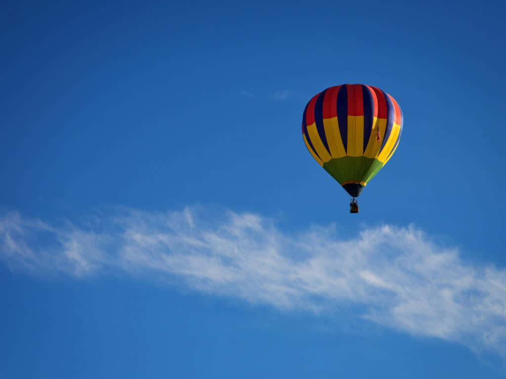 Balloon 桌布 壁紙 — 一個充滿活力的條紋熱氣球在晴朗的藍天中飄浮，伴隨著縷縷白雲。