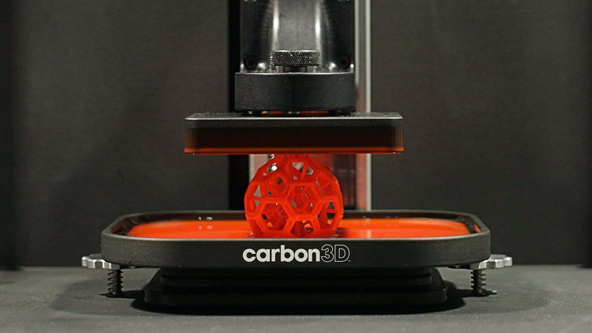 3d Printer 桌布 壁紙 — 一個充滿活力的橙色網格球體正在Carbon 3D打印機上使用樹脂和透明光投影機進行打印中形成。