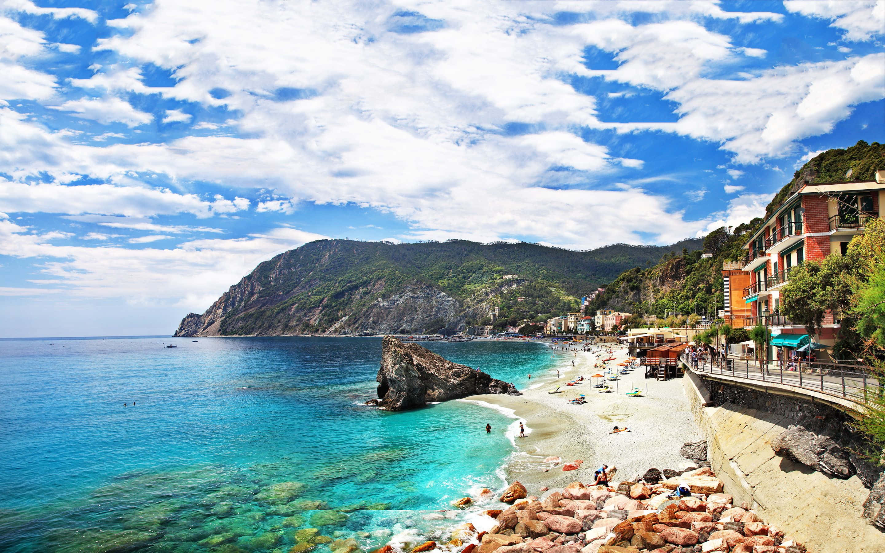 Italian Beach 桌布 壁紙 — 一個充滿活力的海岸沙灘，擁有碧綠的海水和岩石峭壁，在明亮的藍天和蓬鬆的白雲下。