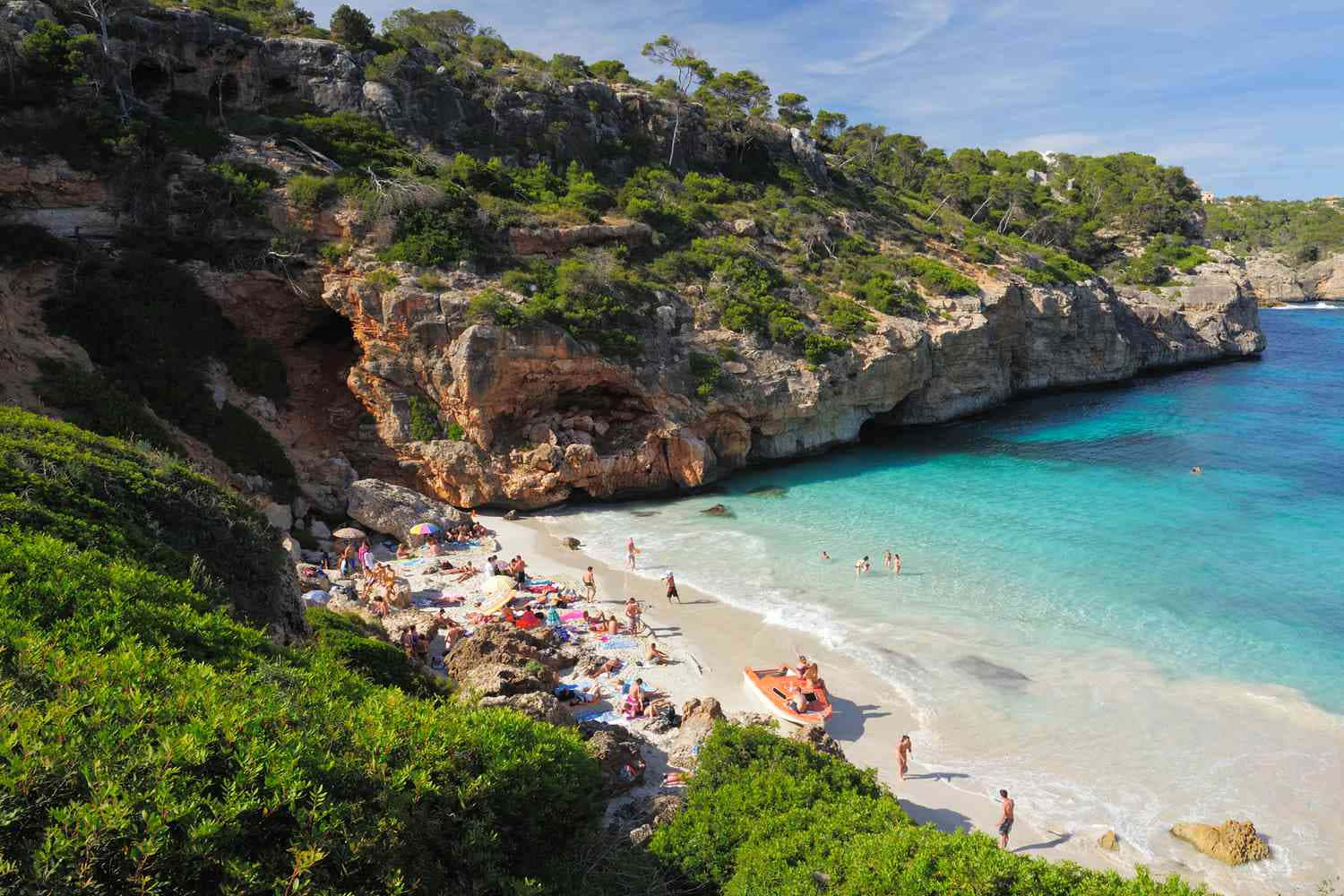 Spanish Beach 桌布 壁紙 — 一個充滿活力的海灣，擁有碧綠的海水、岩石峭壁，點綴著茂密的綠色植物和享受晴朗天氣的日光浴者。