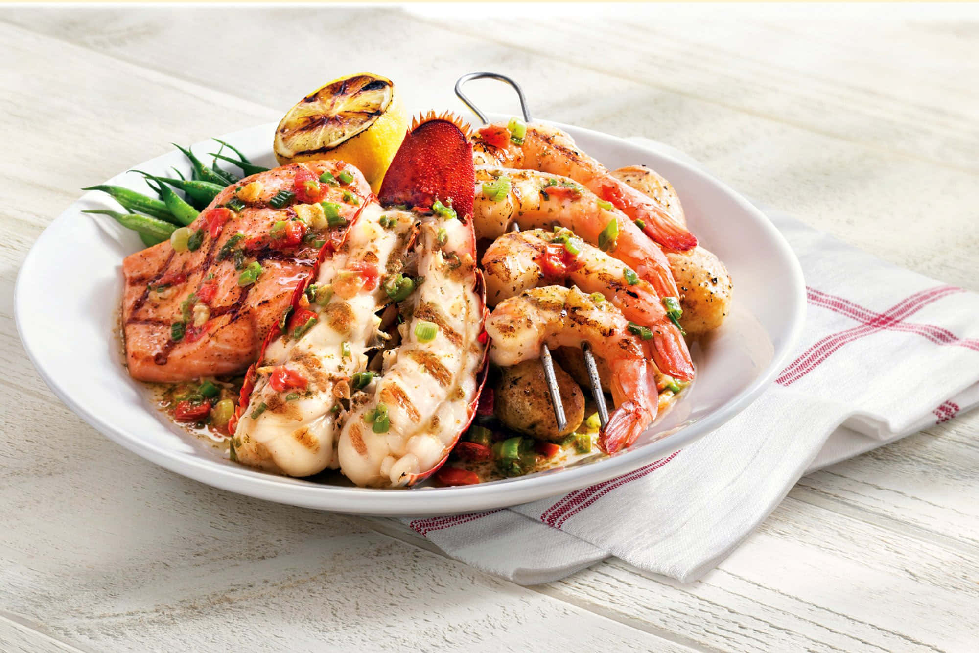 Seafood 桌布 壁紙 — 一個充滿活力的海鮮拼盤，包括烤龍蝦尾、蝦和三文魚，配上紅色醬汁和綠色香草，放在白色盤子上。