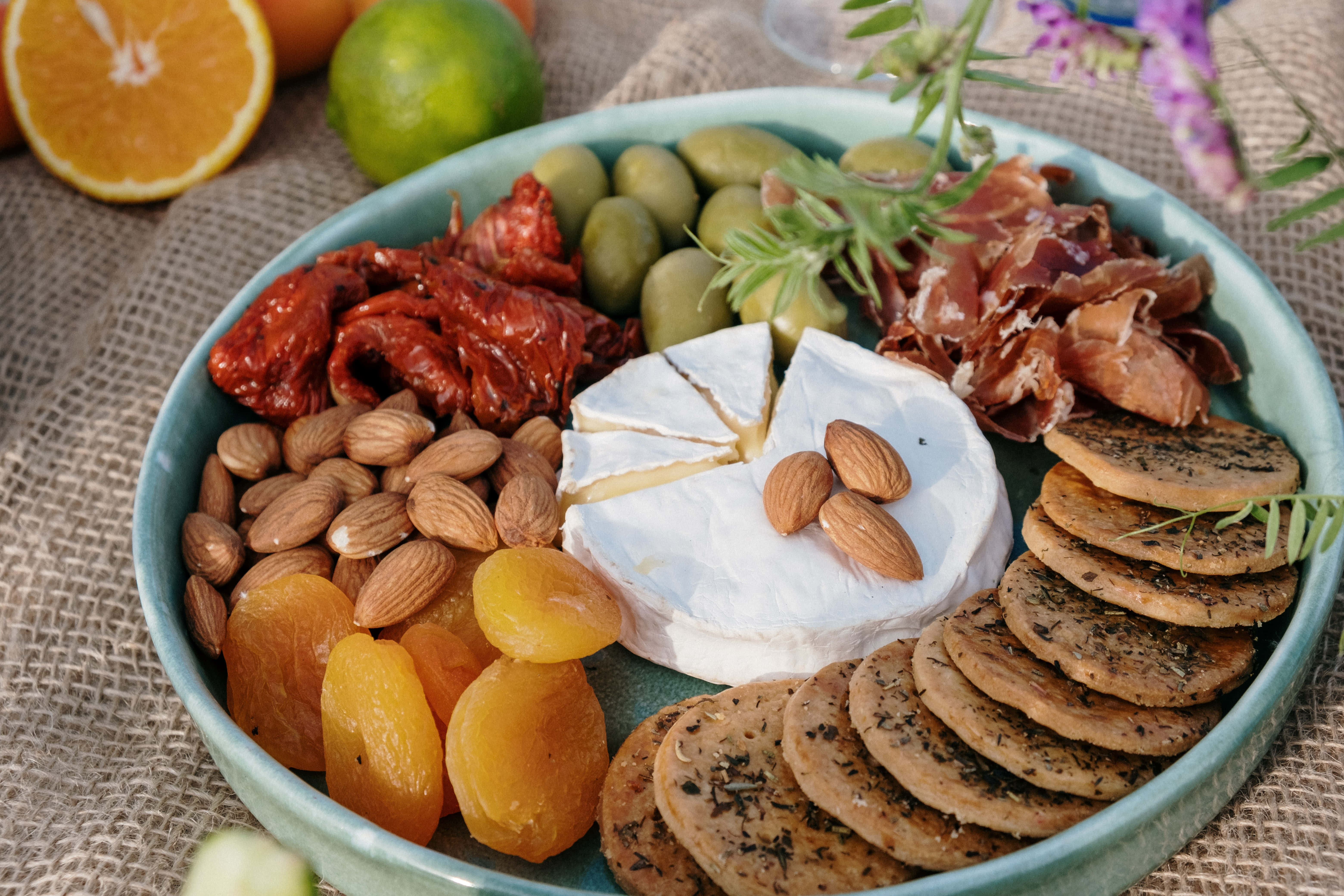 Cheese 桌布 壁紙 — 一個充滿活力的熟食拼盤，上面擺放著芝士、杏仁、橄欖和柑橘類水果，置於質樸的黃麻表面上。