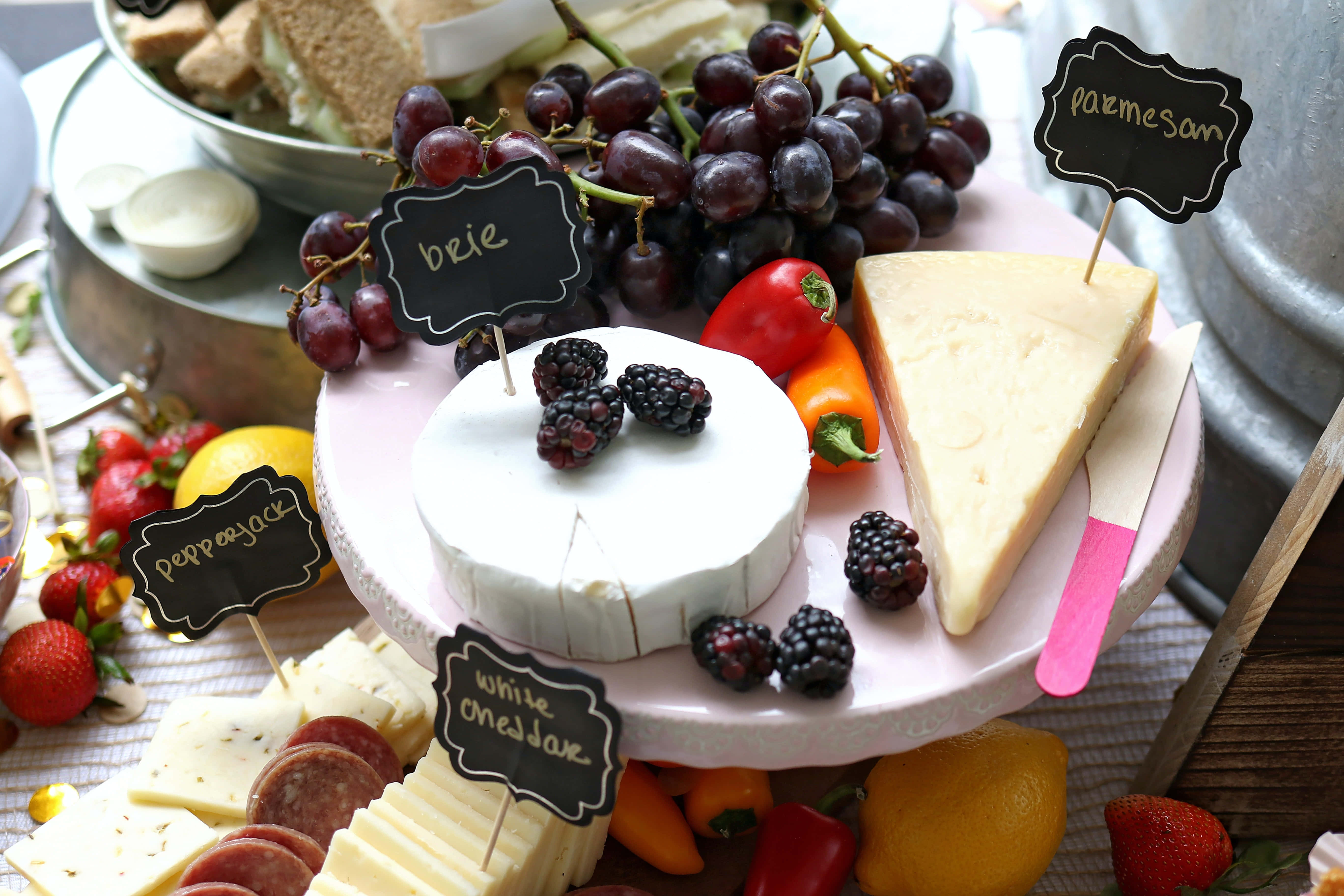 Cheese 桌布 壁紙 — 一個充滿活力的熟食拼盤展示了各種芝士、葡萄、莓果和辣椒，並附有黑板標籤標識每種食物。
