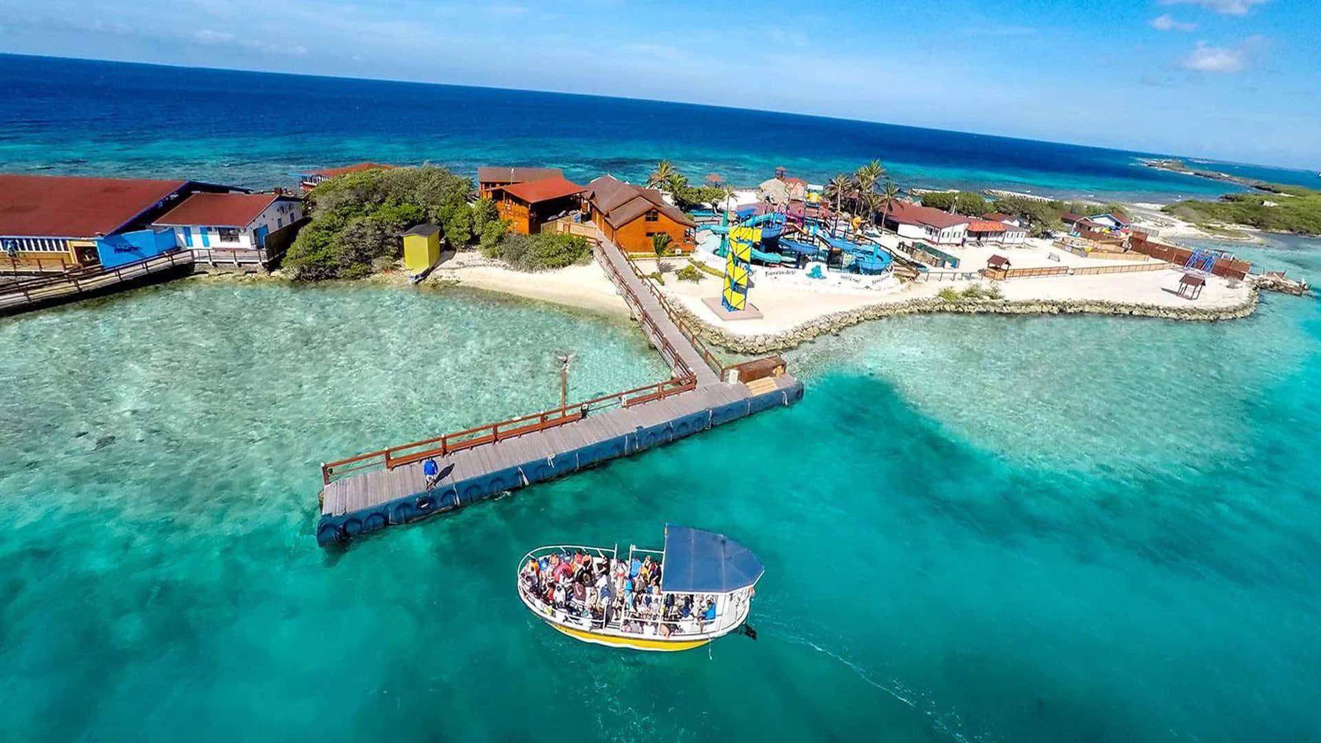 Aruba 桌布 壁紙 — 一個充滿活力的熱帶島嶼度假村的鳥瞰圖，擁有碧綠的海水、木製碼頭和一艘載有客人的觀光船。
