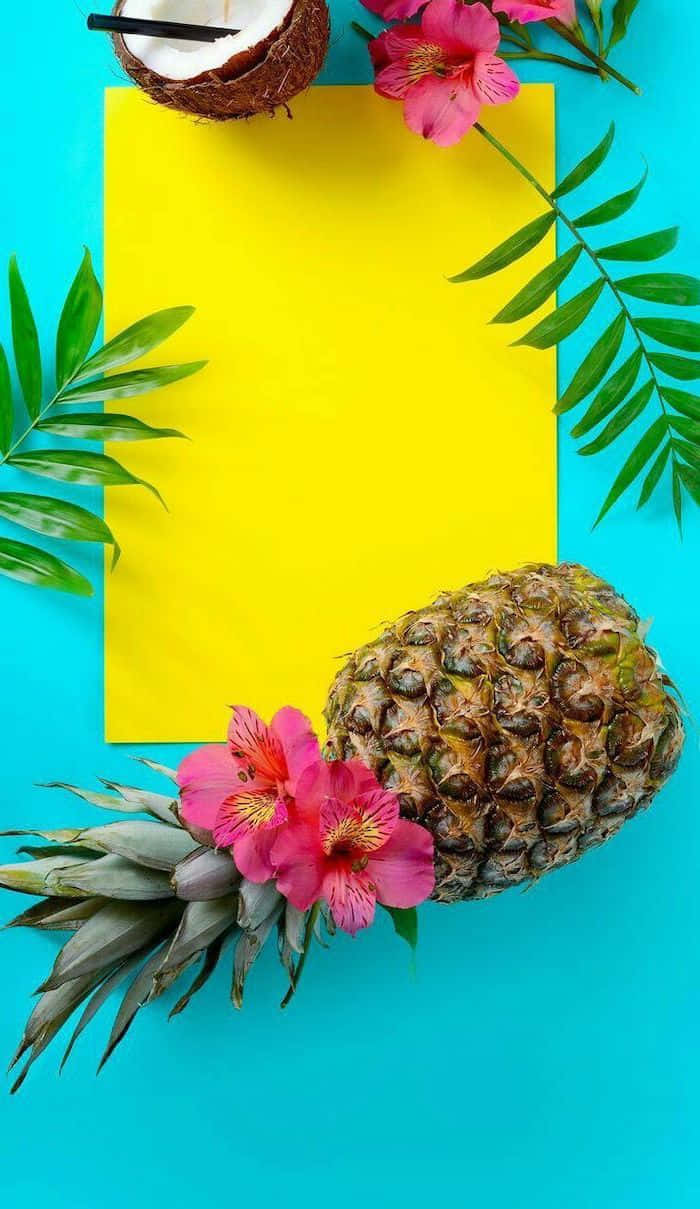 Yellow Summer 桌布 壁紙 — 一個充滿活力的熱帶平鋪構圖，以菠蘿、粉紅花朵、椰子和棕櫚葉圍繞一張黃色卡片，置於藍綠色背景上。