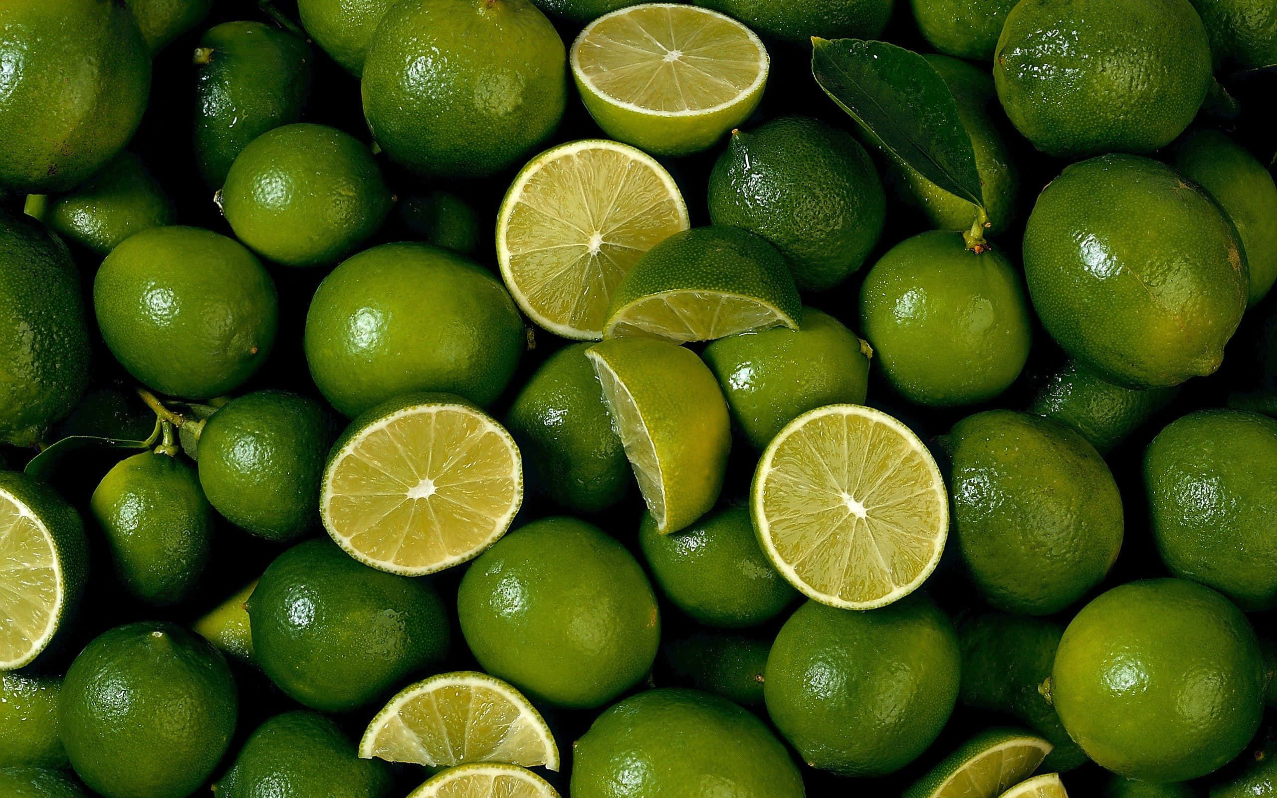 Lime 桌布 壁紙 — 一個充滿活力的特寫，展示完整和切片嘅青檸，表皮光滑，果肉多汁呈黃色。