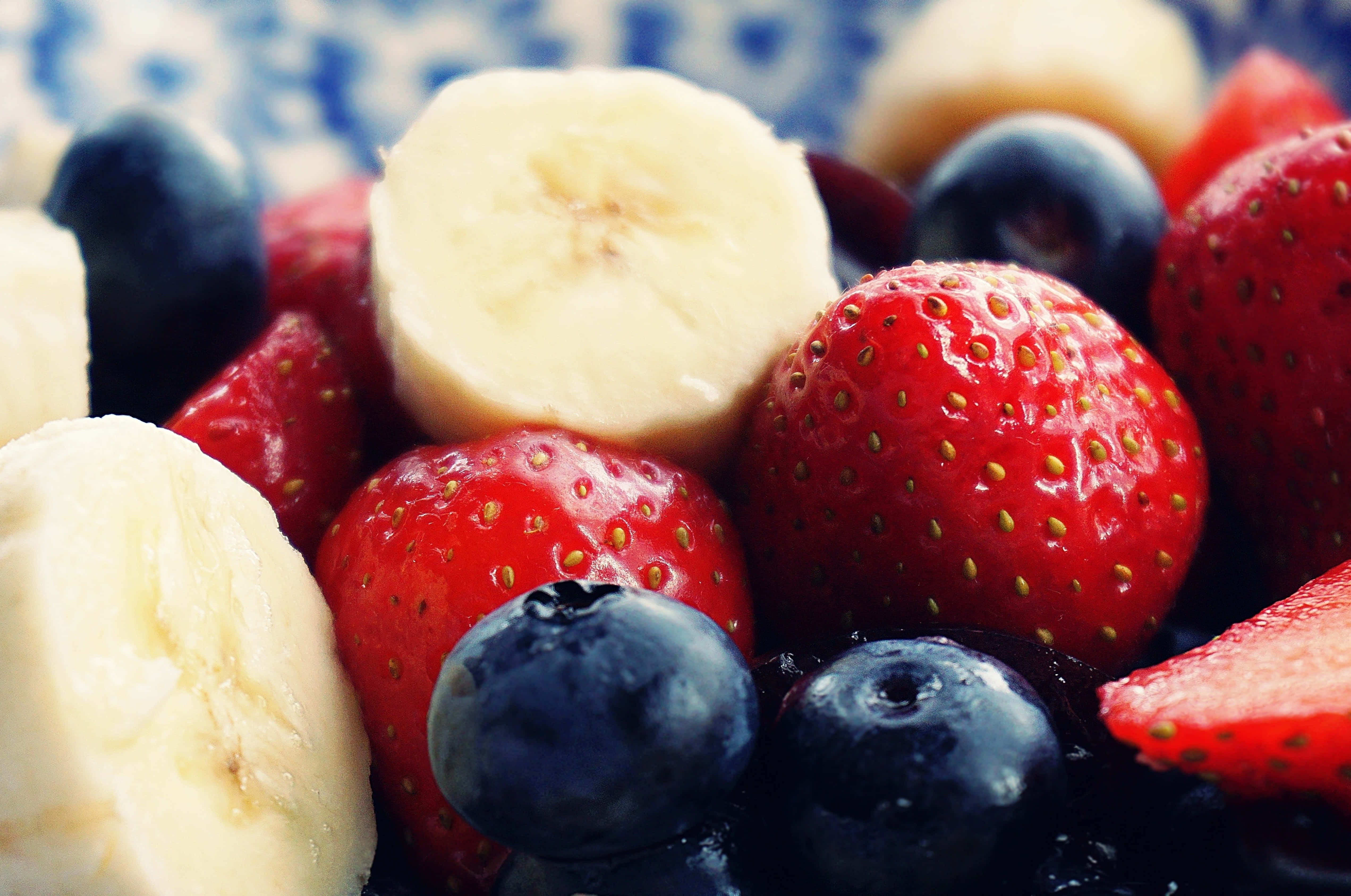 Summer Fruits 桌布 壁紙 — 一個充滿活力的特寫，新鮮切片香蕉、草莓和藍莓整齊排列在一個藍色圖案碟子上。