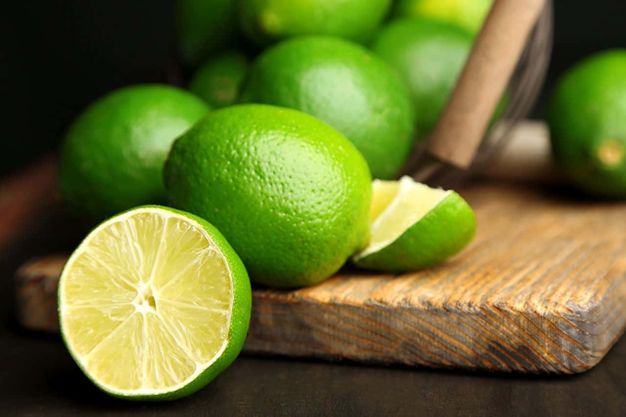Lime 桌布 壁紙 — 一個充滿活力的特寫，新鮮青檸放在質樸的木砧板上，其中一個切開露出多汁的果肉。
