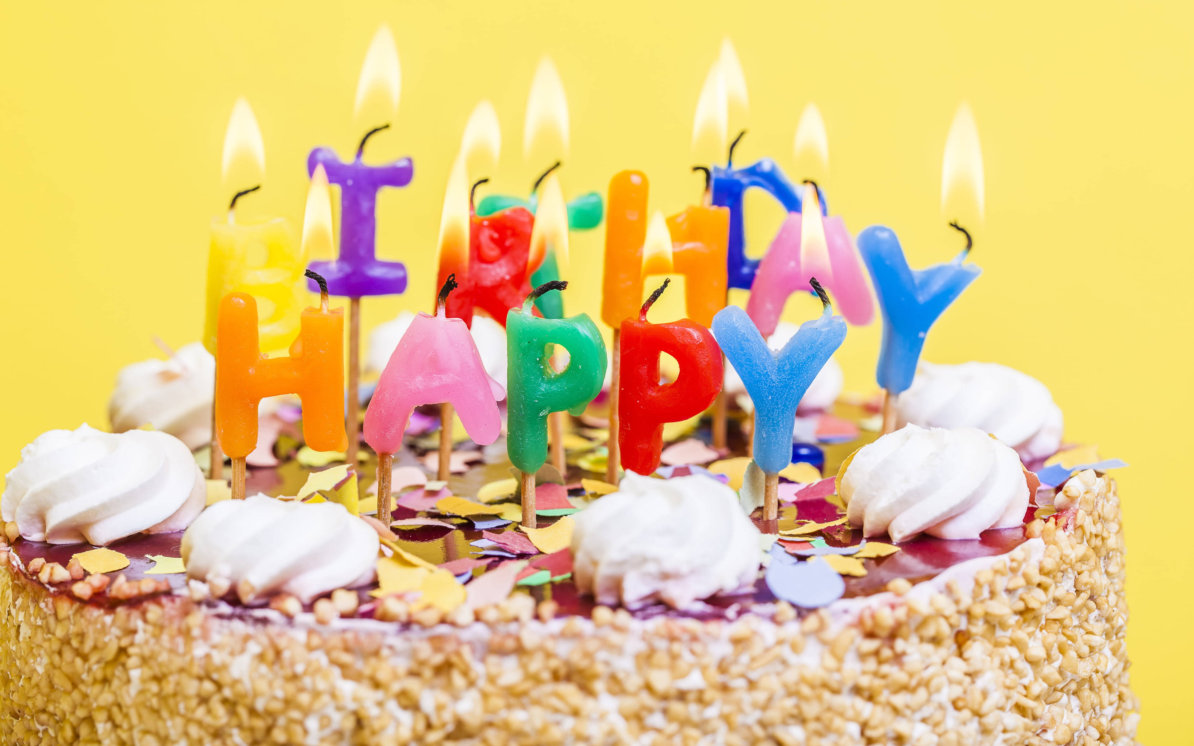 Birthday 桌布 壁紙 — 一個充滿活力的生日蛋糕，上面裝飾著彩色字母蠟燭拼出 'HAPPY' 和忌廉，背景是明亮的黃色。